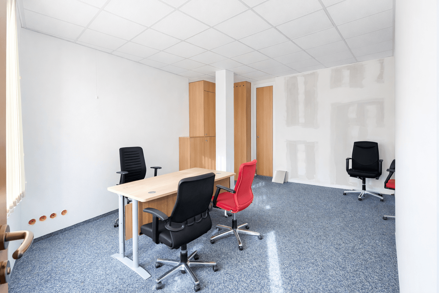 Geräumiges Büro mit Teppichboden, Holzschränken und einem Bereich, der noch fertiggestellt werden muss.