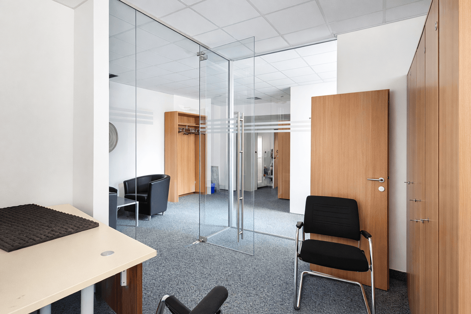 Moderner Bürogang mit Glaswänden, Holztüren und Teppichboden, der zu weiteren Räumen führt.