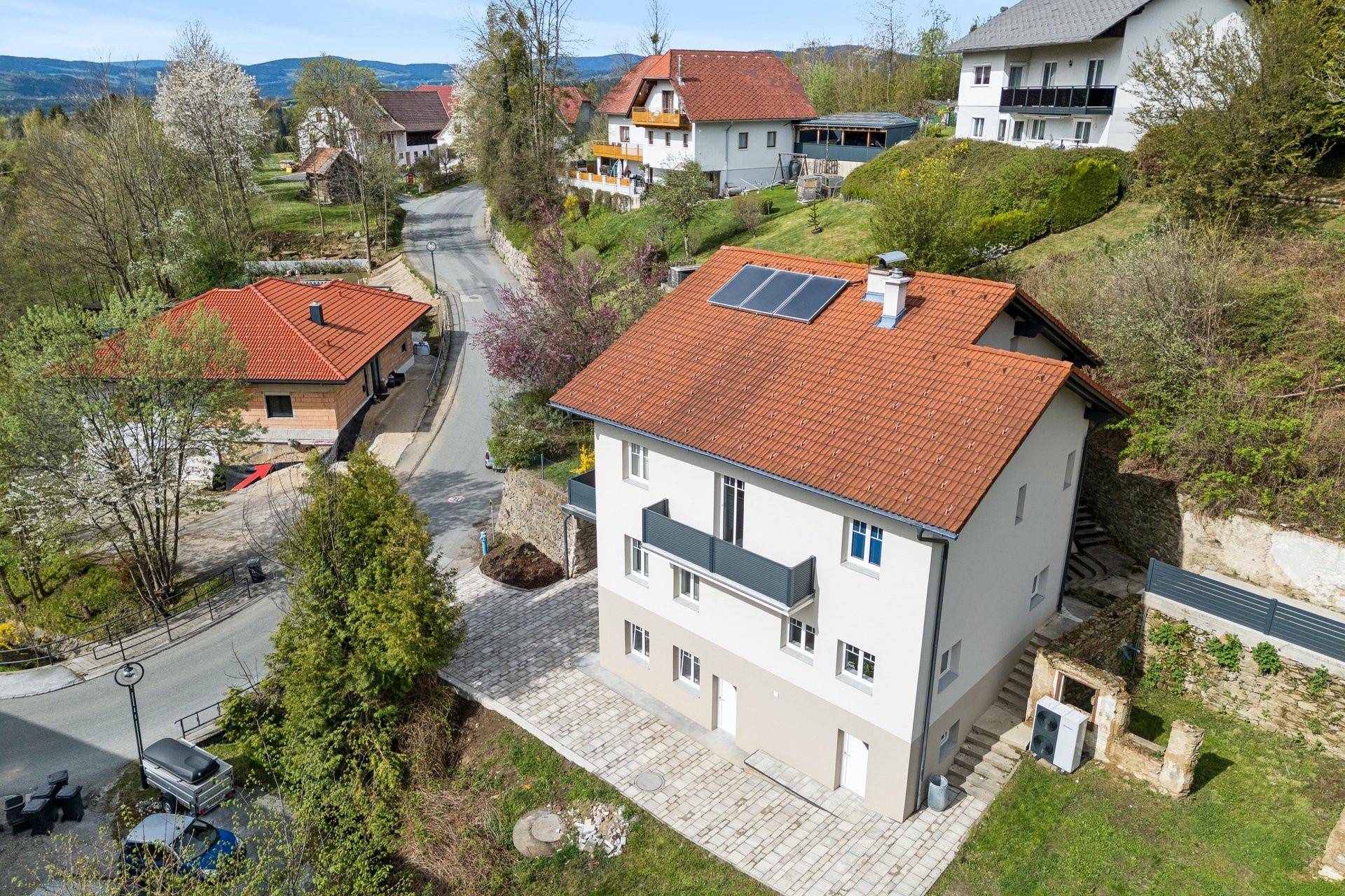 Luftaufnahme eines Wohnhauses mit Ziegeldach und Photovoltaikanlage in einer ländlichen Umgebung.