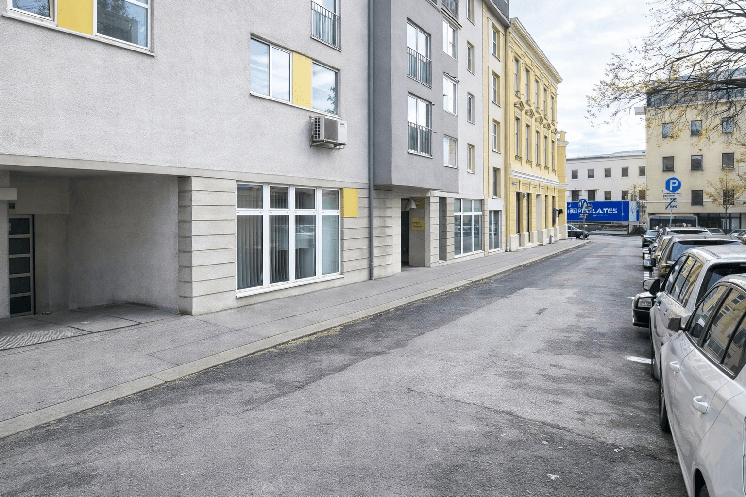 Straßenansicht eines modernen Bürogebäudes mit Geschäften im Erdgeschoss und parkenden Autos.
