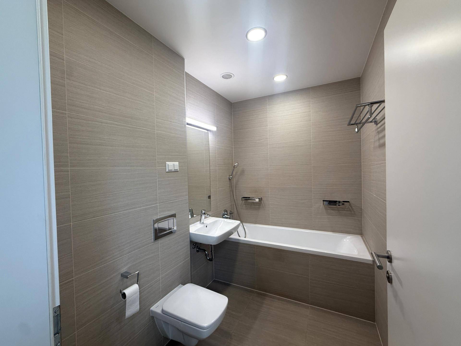 Modernes Badezimmer mit grauen Fliesen, Badewanne, wandhängendem WC und Einzelwaschbecken.