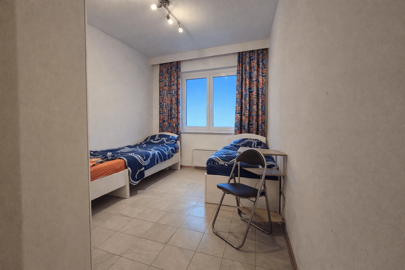 Helles Schlafzimmer mit zwei Einzelbetten, Fliesenboden und Fenster.
