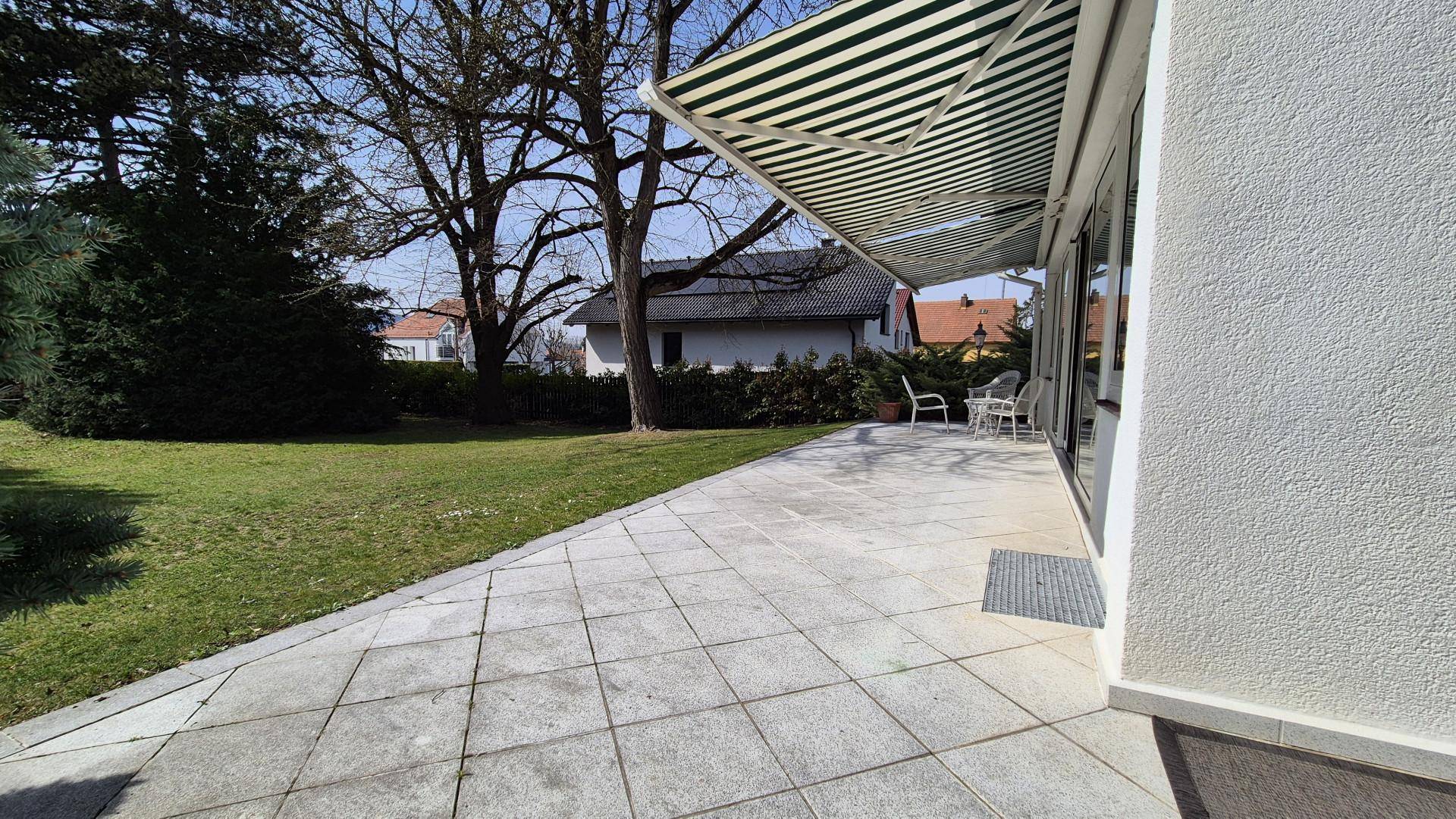 Große gepflasterte Terrasse mit Markise und Blick auf den weitläufigen Garten.