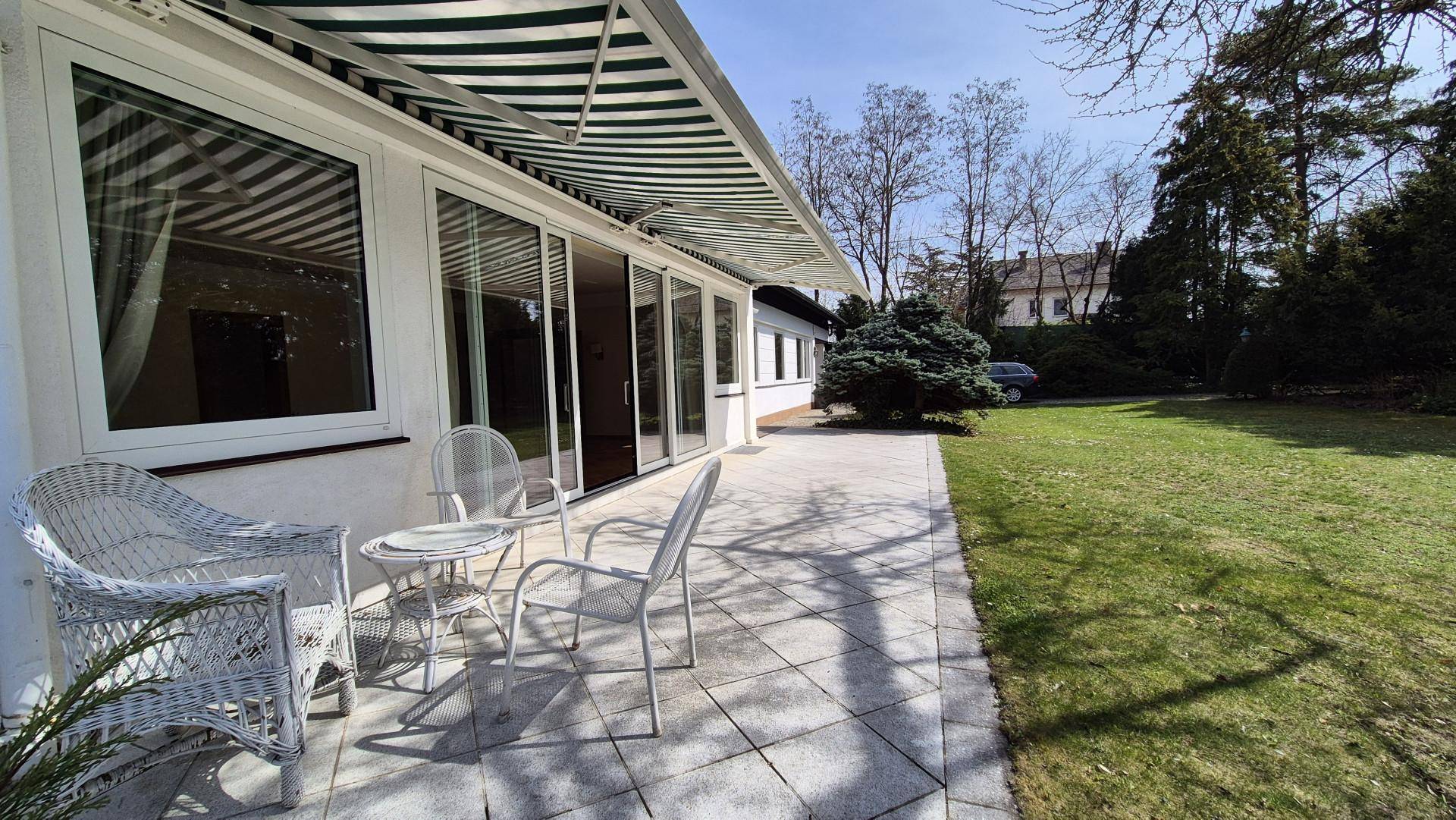 Sonniger Terrassenbereich mit Gartenmöbeln, Markise und Zugang zum Garten.