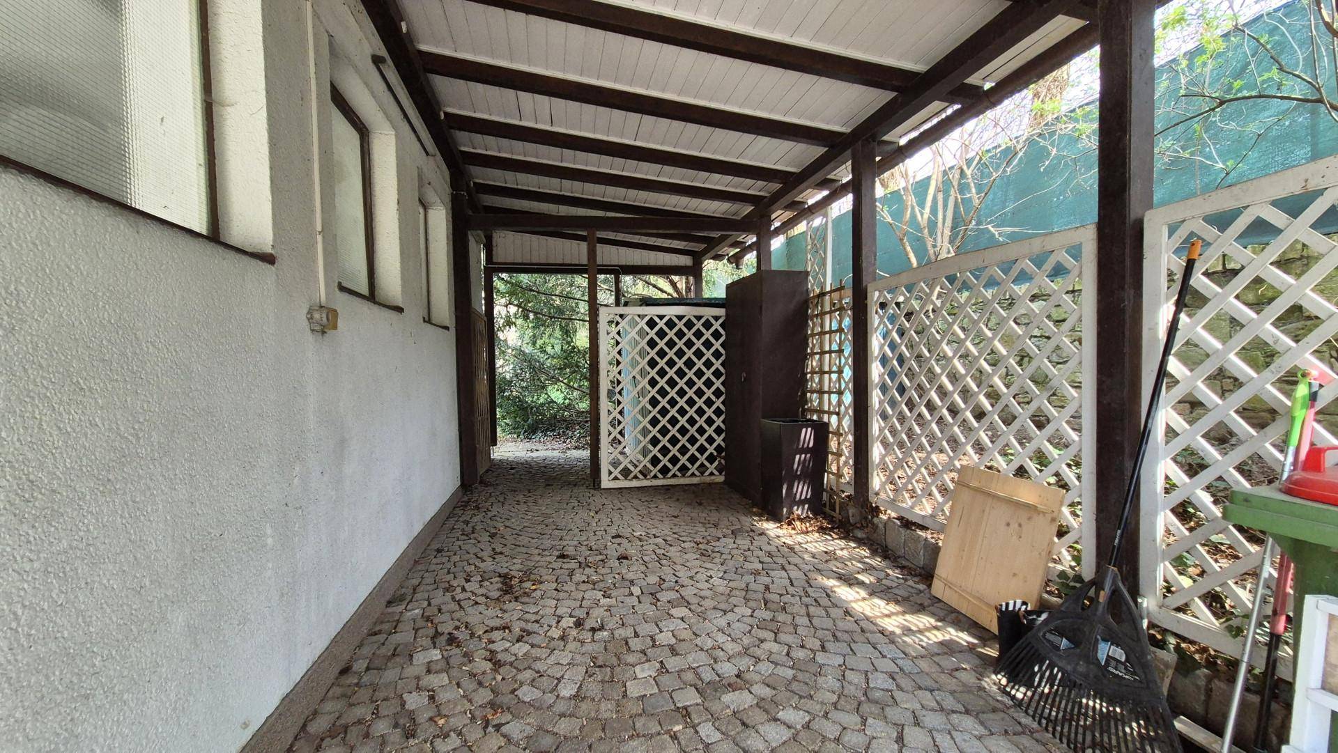 Überdachter Stellplatz oder Carport mit gepflastertem Boden und Stauraum.