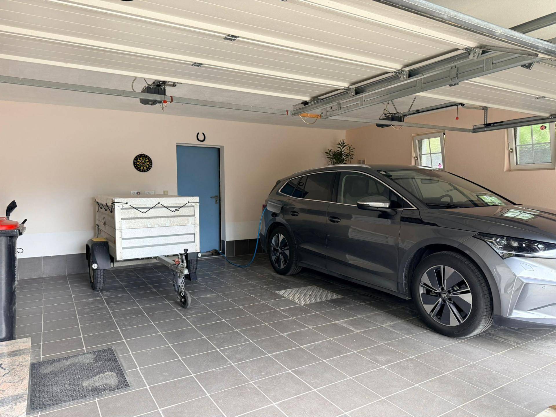 Geräumige Garage mit Fliesenboden, Platz für ein Fahrzeug und einem Anhänger sowie EV-Ladestation.