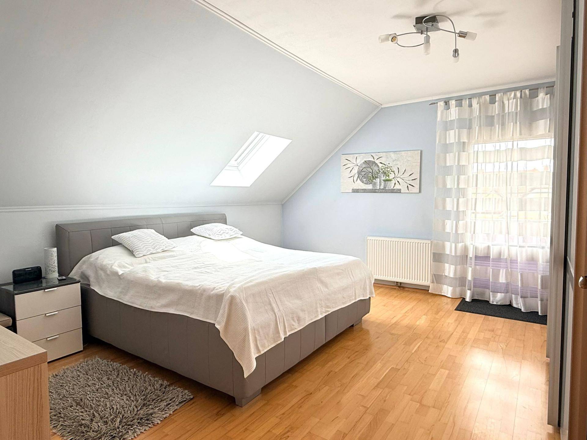 Gemütliches Schlafzimmer mit Doppelbett, Parkettboden und Dachfenster, in hellen Farbtönen gehalten.