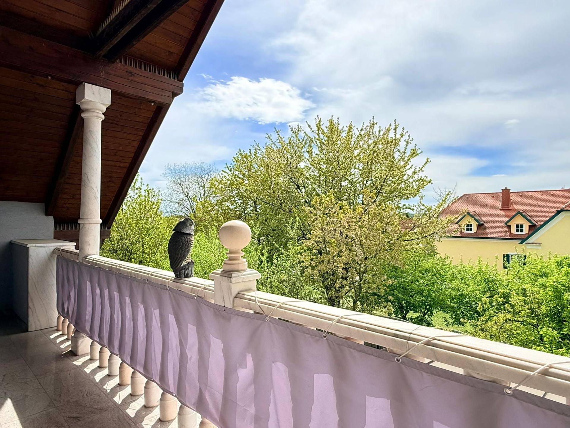 Balkon mit weitem Blick ins Grüne und auf die umliegende Wohnbebauung unter blauem Himmel.