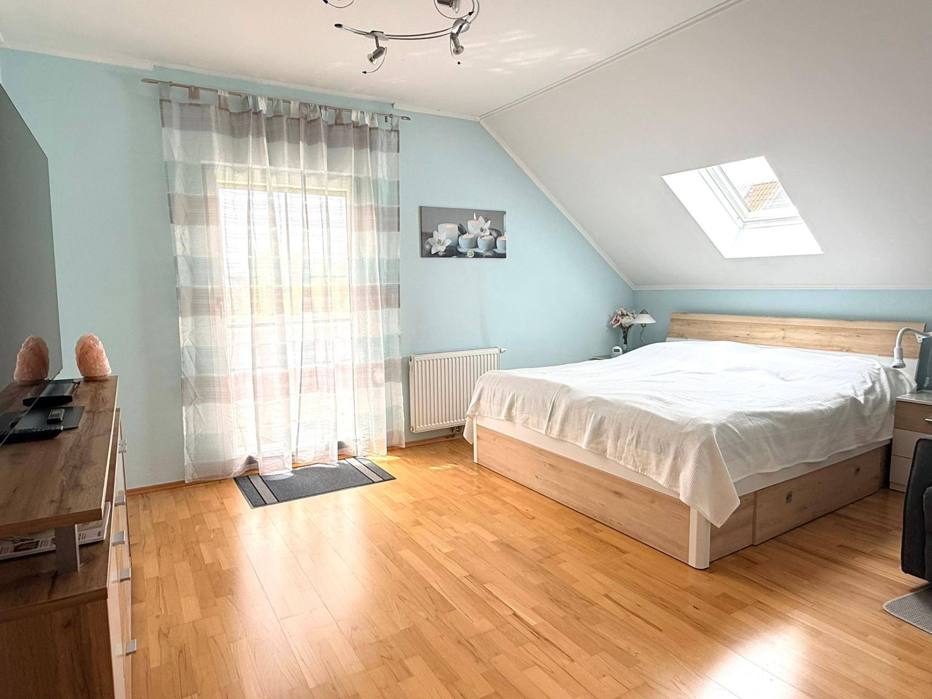 Helles Schlafzimmer mit Holzbett, Parkettboden und Dachschräge, durchflutet von natürlichem Licht.