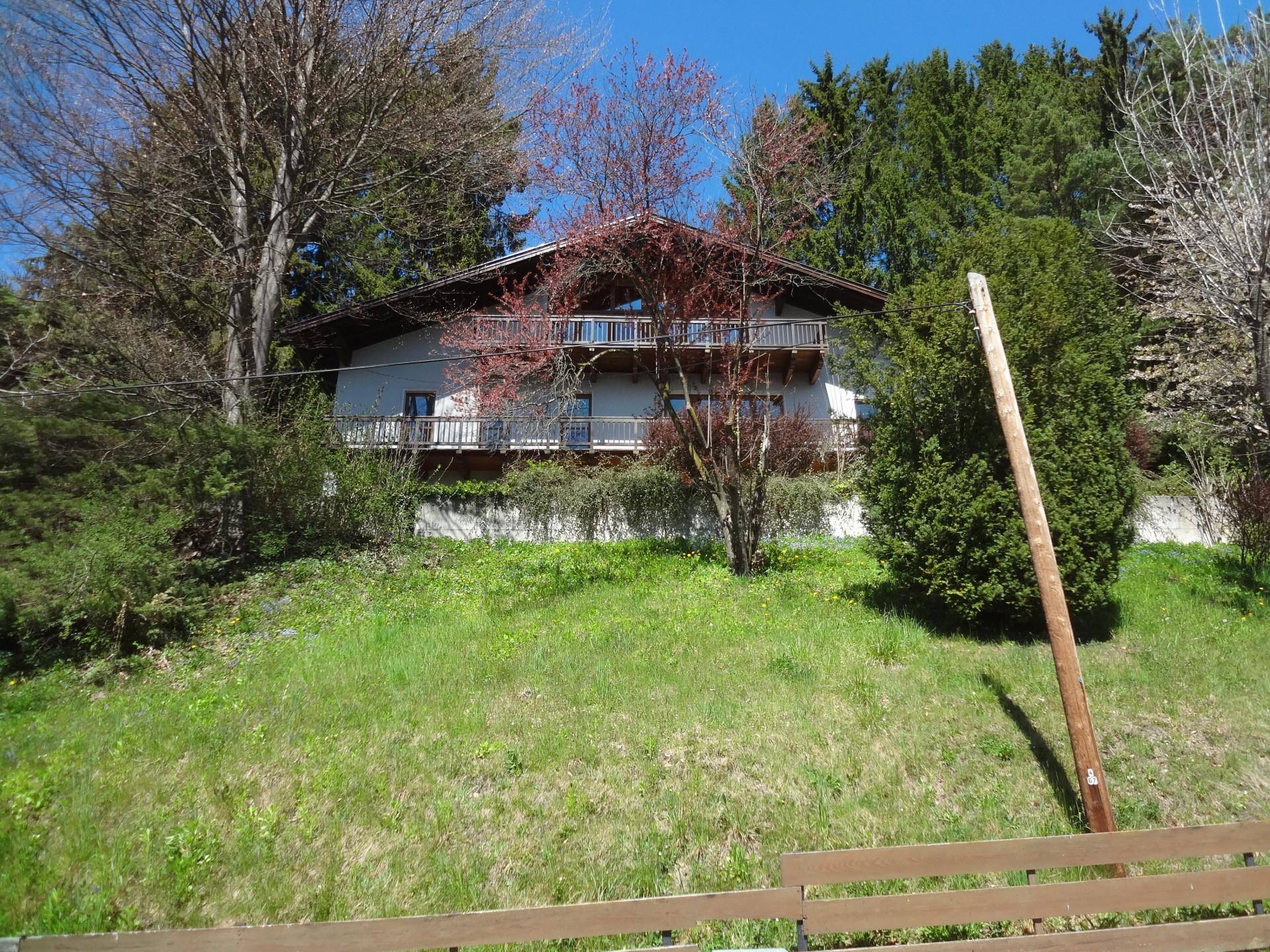 Wohnhaus mit mehreren Balkonen, eingebettet in eine grüne Hügellandschaft mit Bäumen.