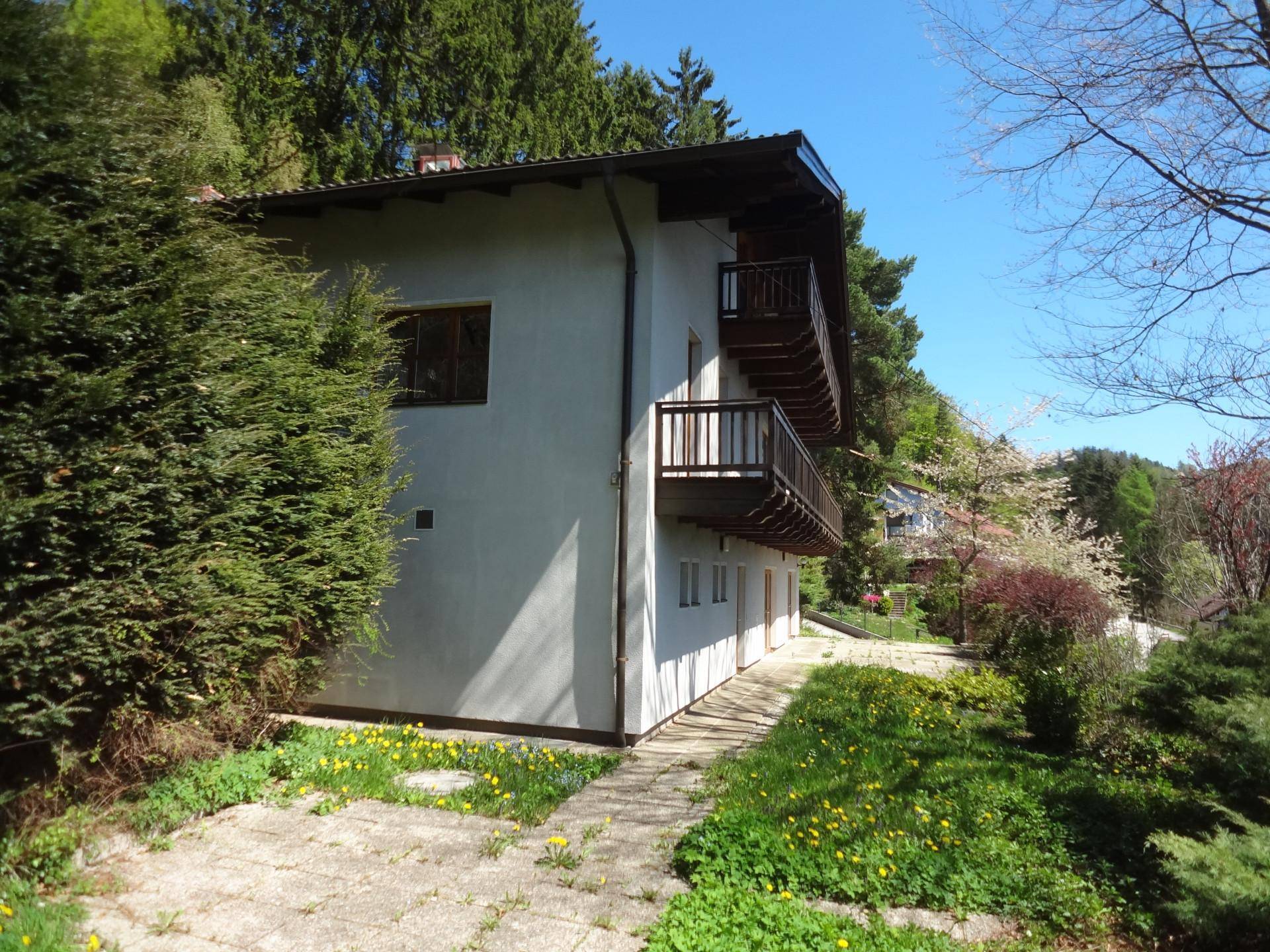 Gebäude mit Holzbalkonen und weißer Fassade, umgeben von einer grünen Wiese und Bäumen.