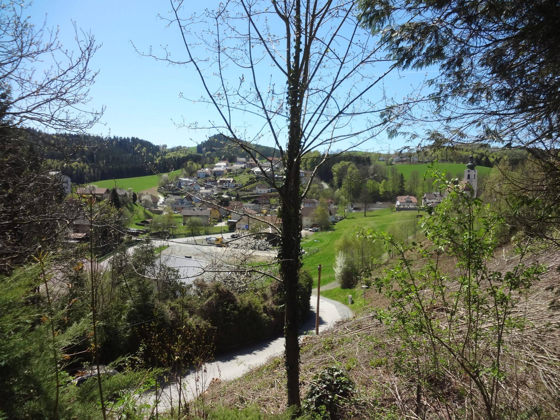 Panoramablick auf ein malerisches Dorf in einer grünen Hügellandschaft unter blauem Himmel.