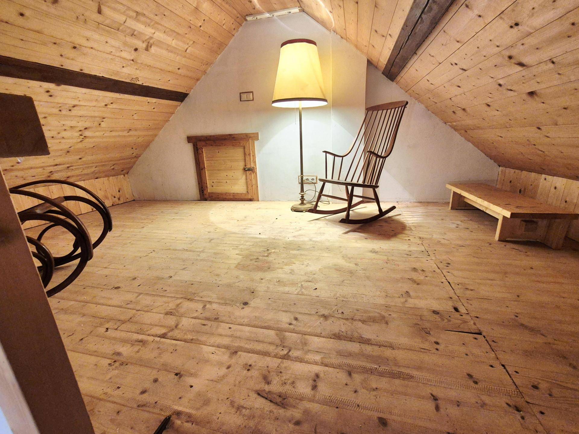 Dachbodenraum mit schrägen Wänden, Holzverkleidung und einem Schaukelstuhl unter einer Stehlampe.