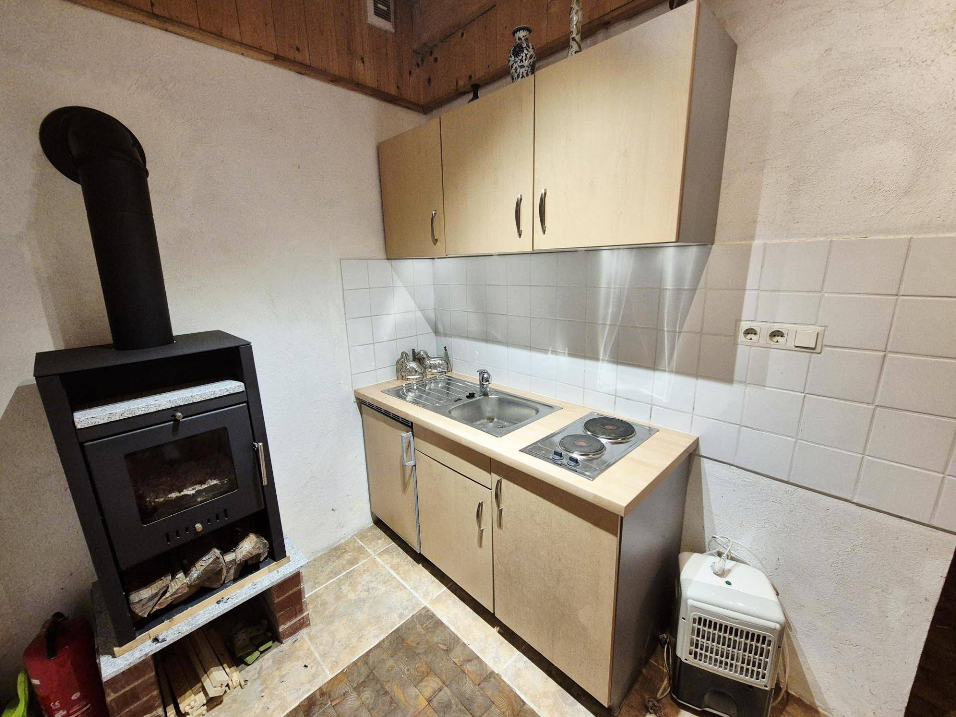 Kleine Küche mit Holzofen, einfachen Schränken und einer Kochplatte in rustikalem Ambiente.