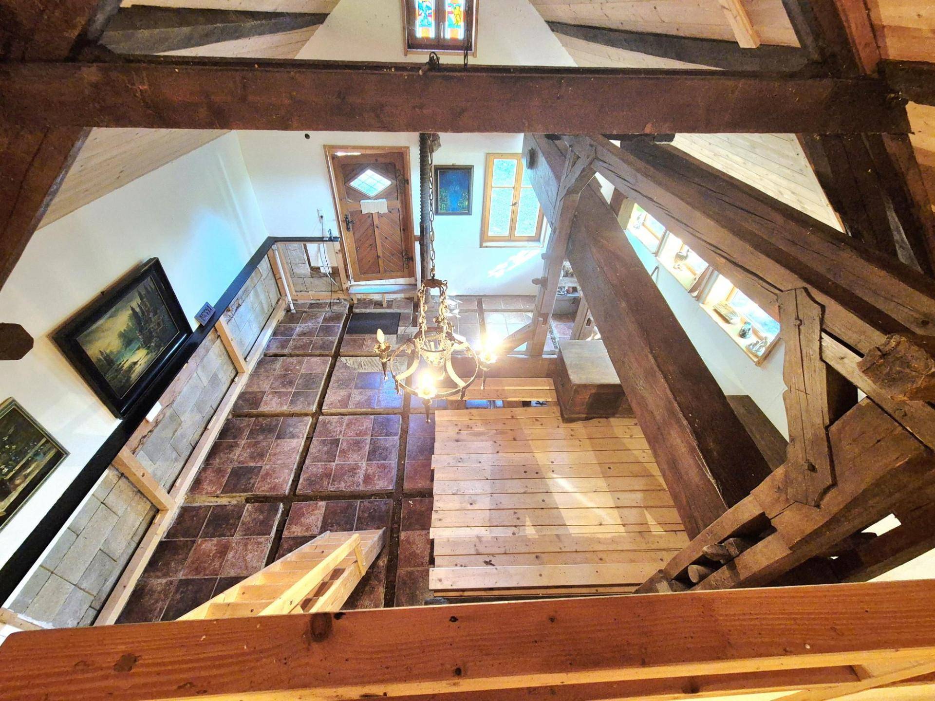 Blick von oben auf einen Wohnbereich mit Holzbalken, Fliesenboden und einer antiken Lampe.