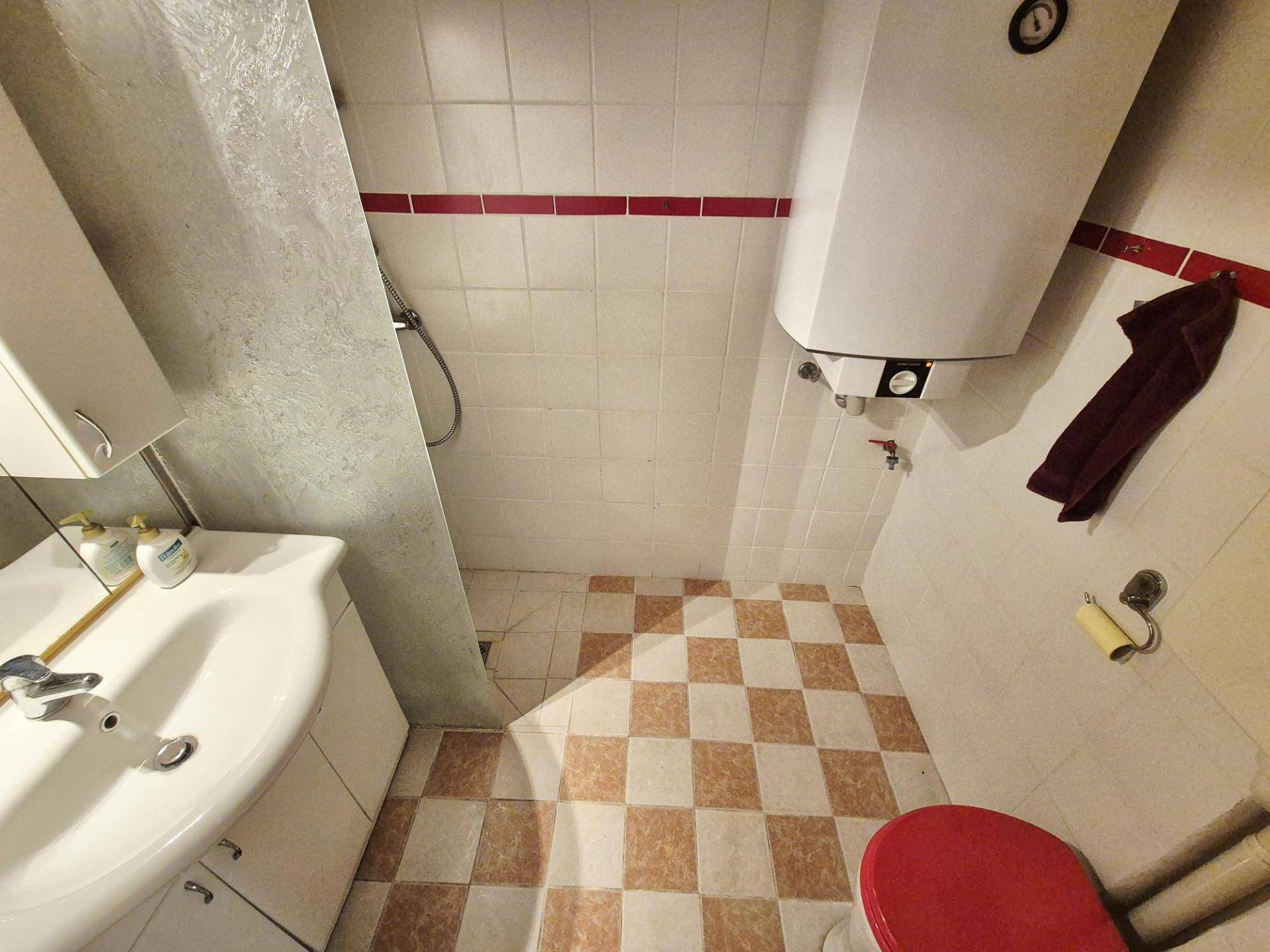 Kleines Badezimmer mit karierten Fliesen, Dusche und einem roten Toilettensitz.