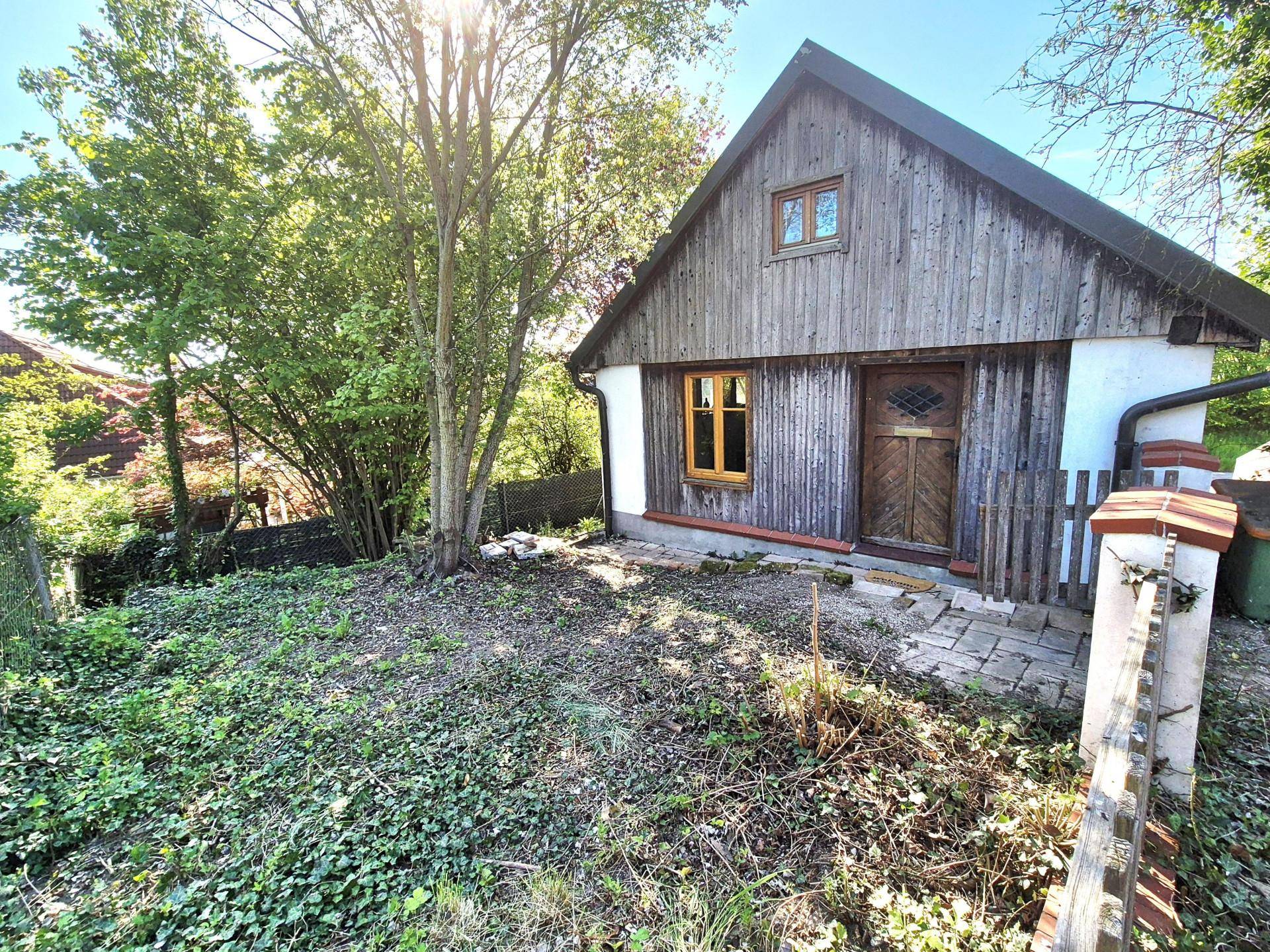 Kleiner Gartenbereich vor einem rustikalen Gebäude mit Holzverkleidung und viel Grün.