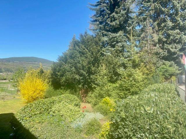 Üppiger Garten mit verschiedenen Bäumen, Sträuchern und weitem Blick in die Natur.