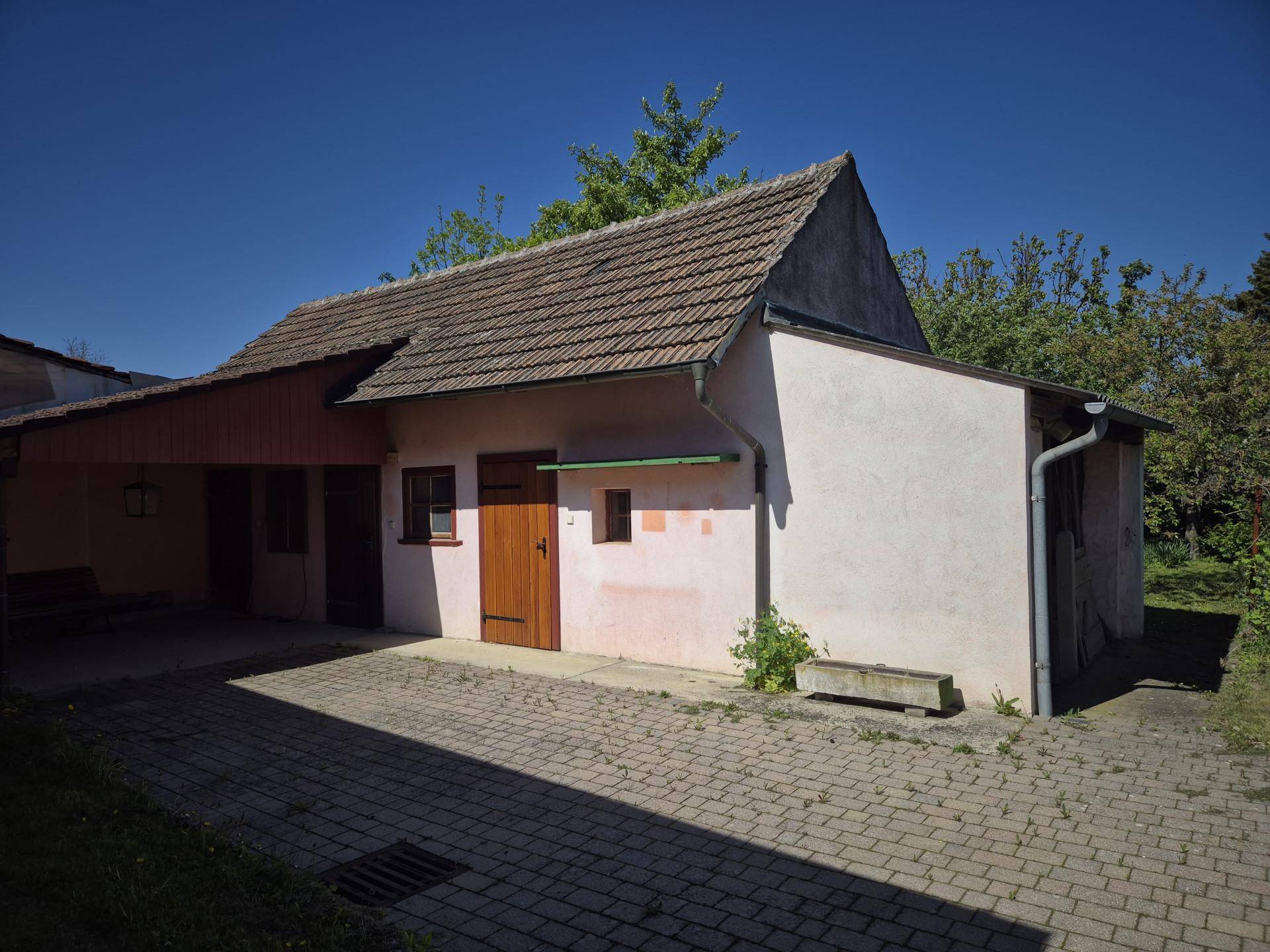 Nebengebäude mit überdachtem Carport und gepflastertem Hofbereich bei Sonnenschein.