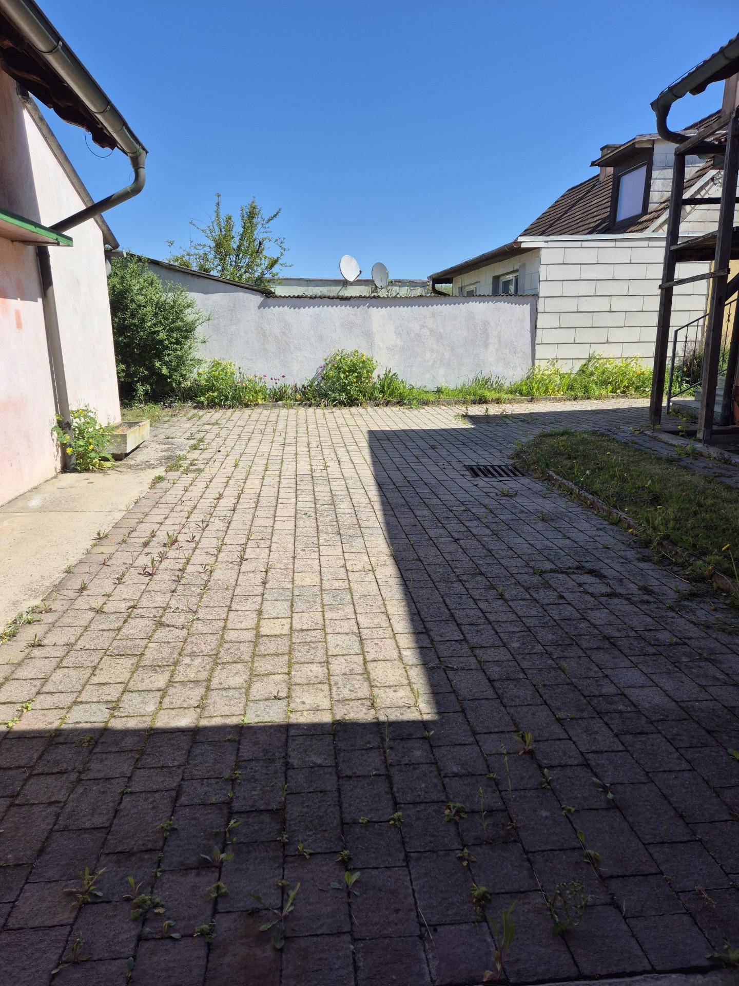 Gepflasterter Hofbereich zwischen Gebäuden mit einer Mauer im Hintergrund unter blauem Himmel.