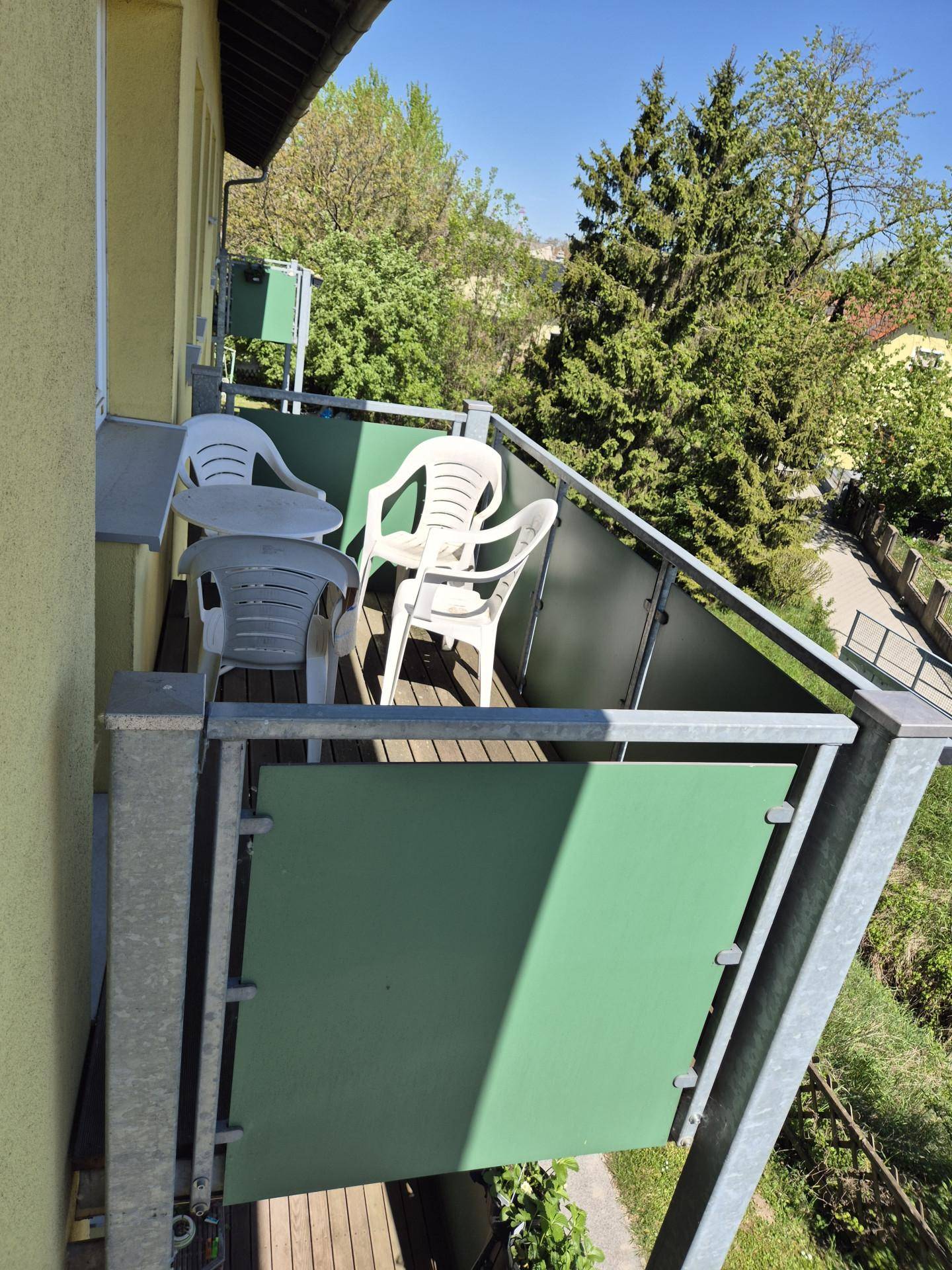 Kleiner Balkon mit Sitzgelegenheiten und Blick auf Bäume und die Umgebung.