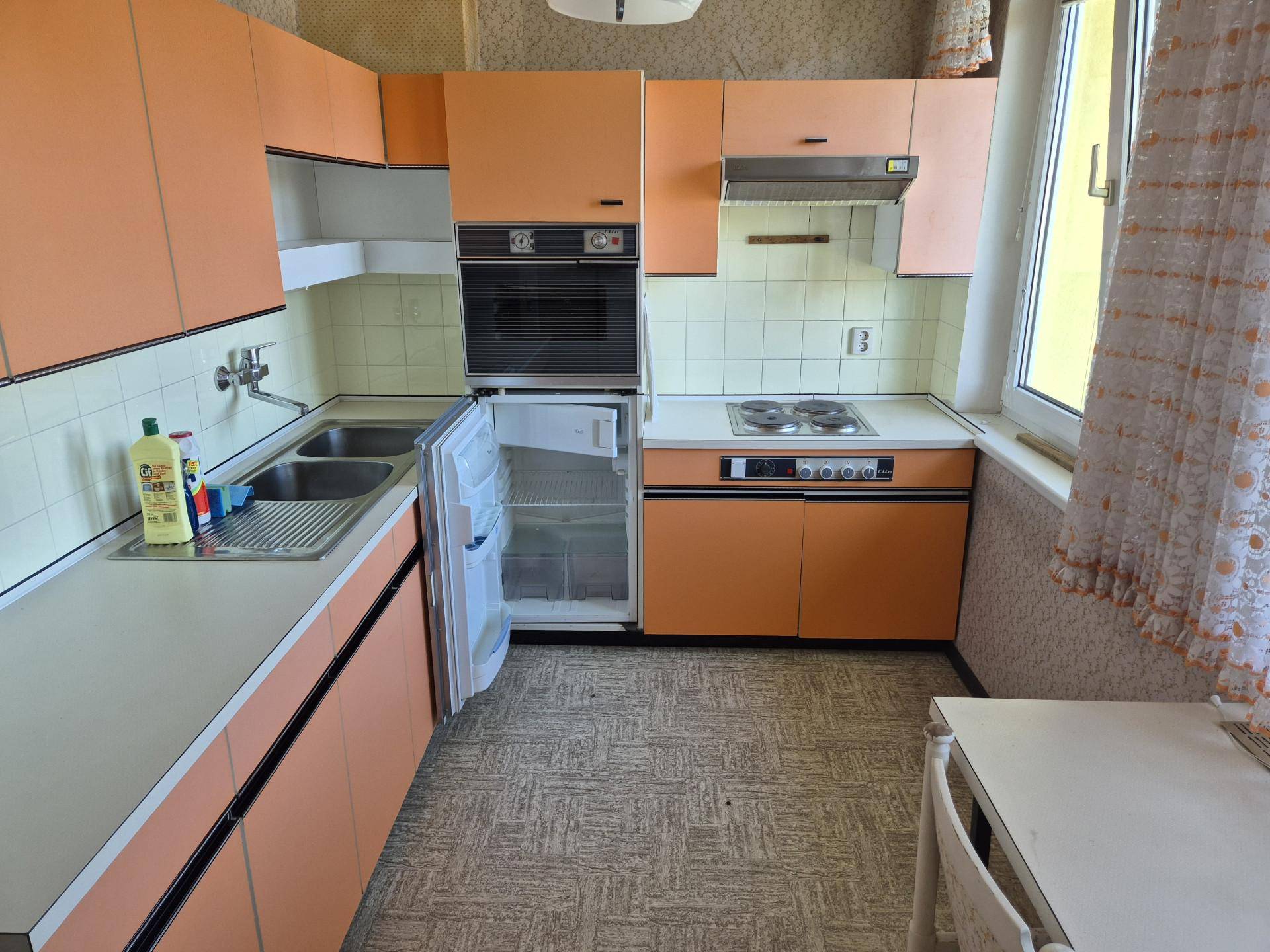 Funktionale Küche im Retro-Stil mit orangefarbenen Schränken, Einbaugeräten und Fenster.