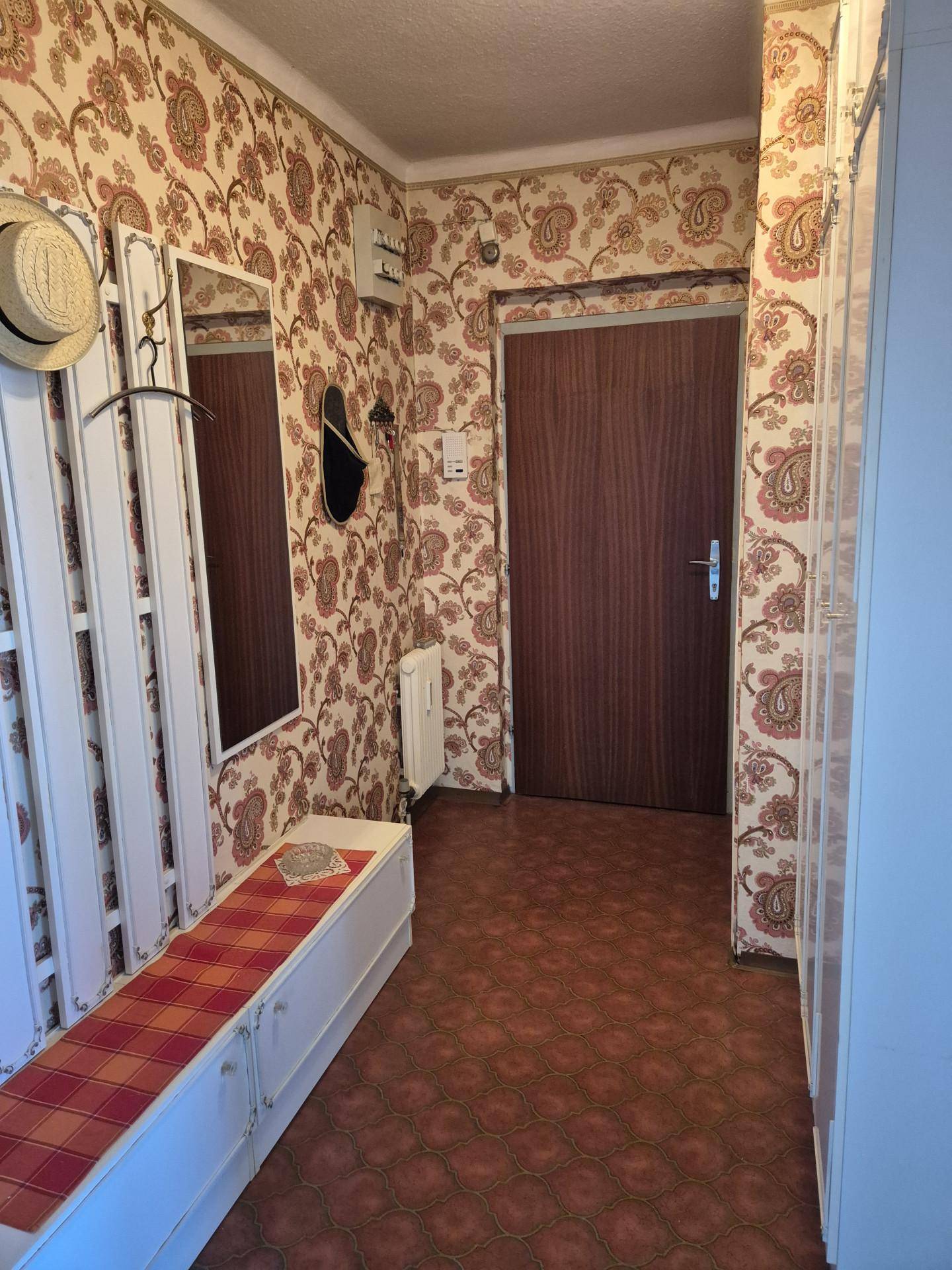 Flur mit auffälliger gemusterter Tapete, Garderobe und Spiegel.