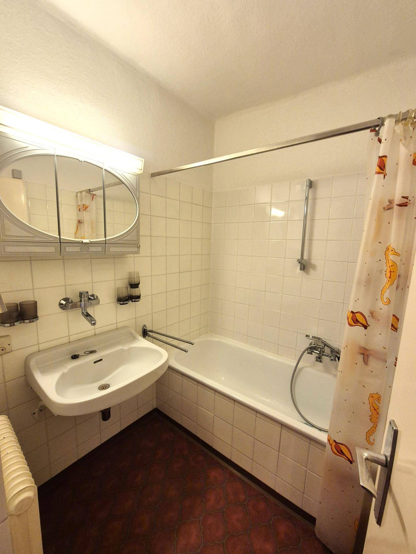 Badezimmer mit Badewanne, Waschbecken, Spiegelschrank und weißen Fliesen.