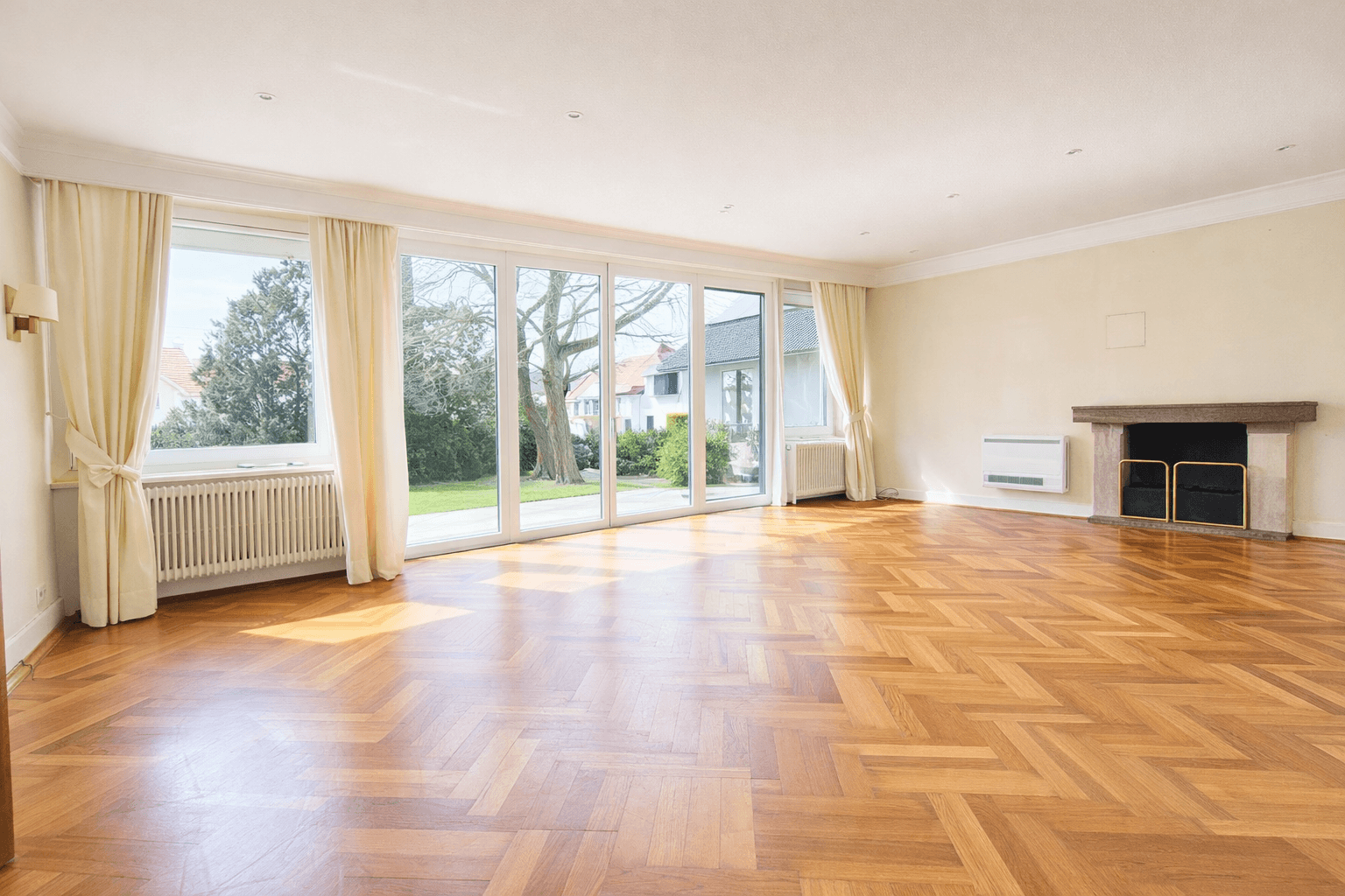 Helles Wohnzimmer mit Fischgrätparkett, großzügigen Fensterfronten und einem Kamin.