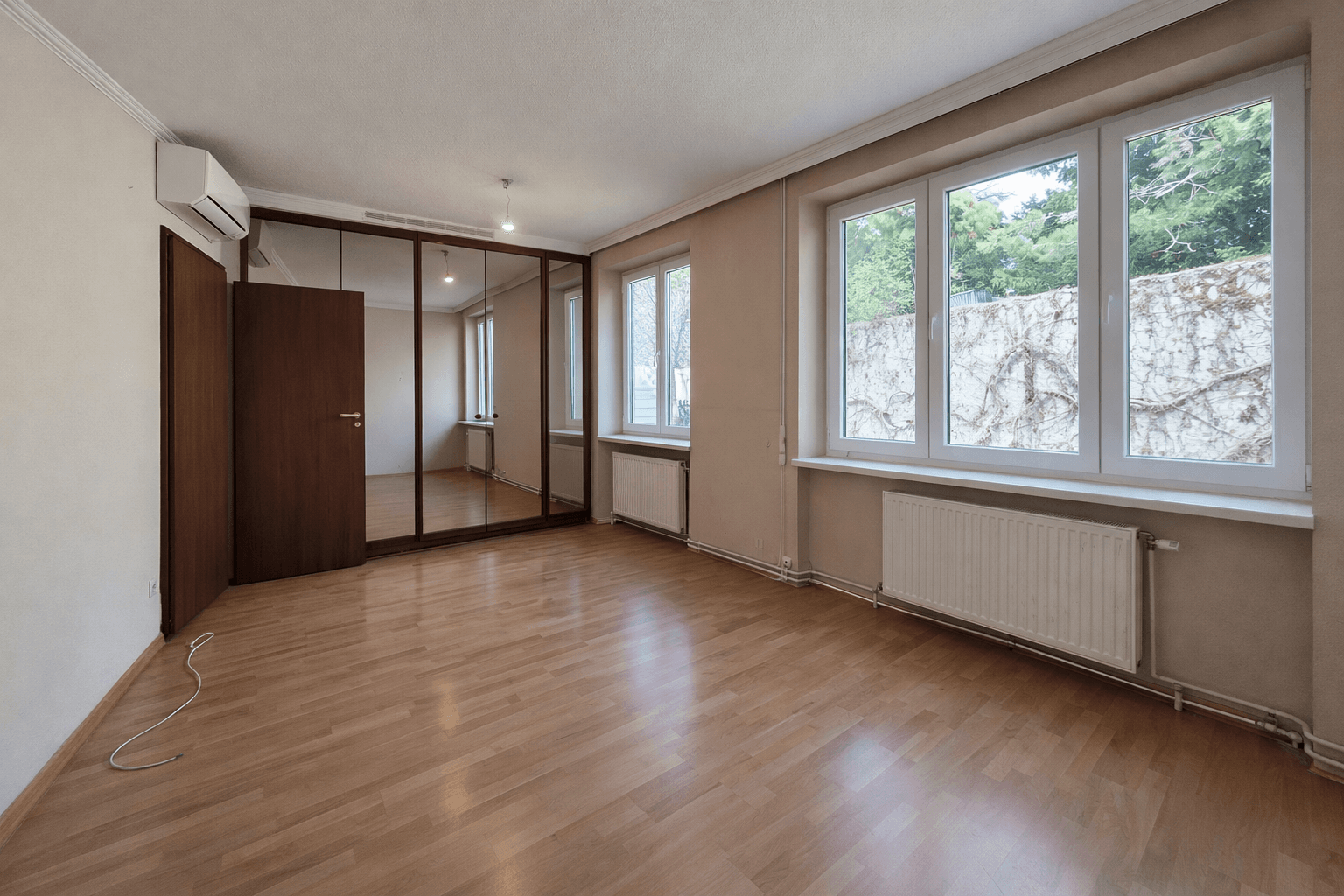 Schlafzimmer mit Spiegelschränken, Laminatboden und großen Fenstern zum Garten.