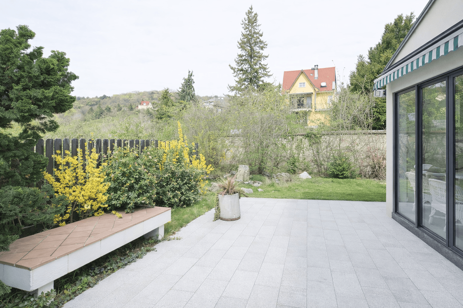 Sonniger Terrassenbereich mit Sitzbank und Blick auf die grüne Umgebung.