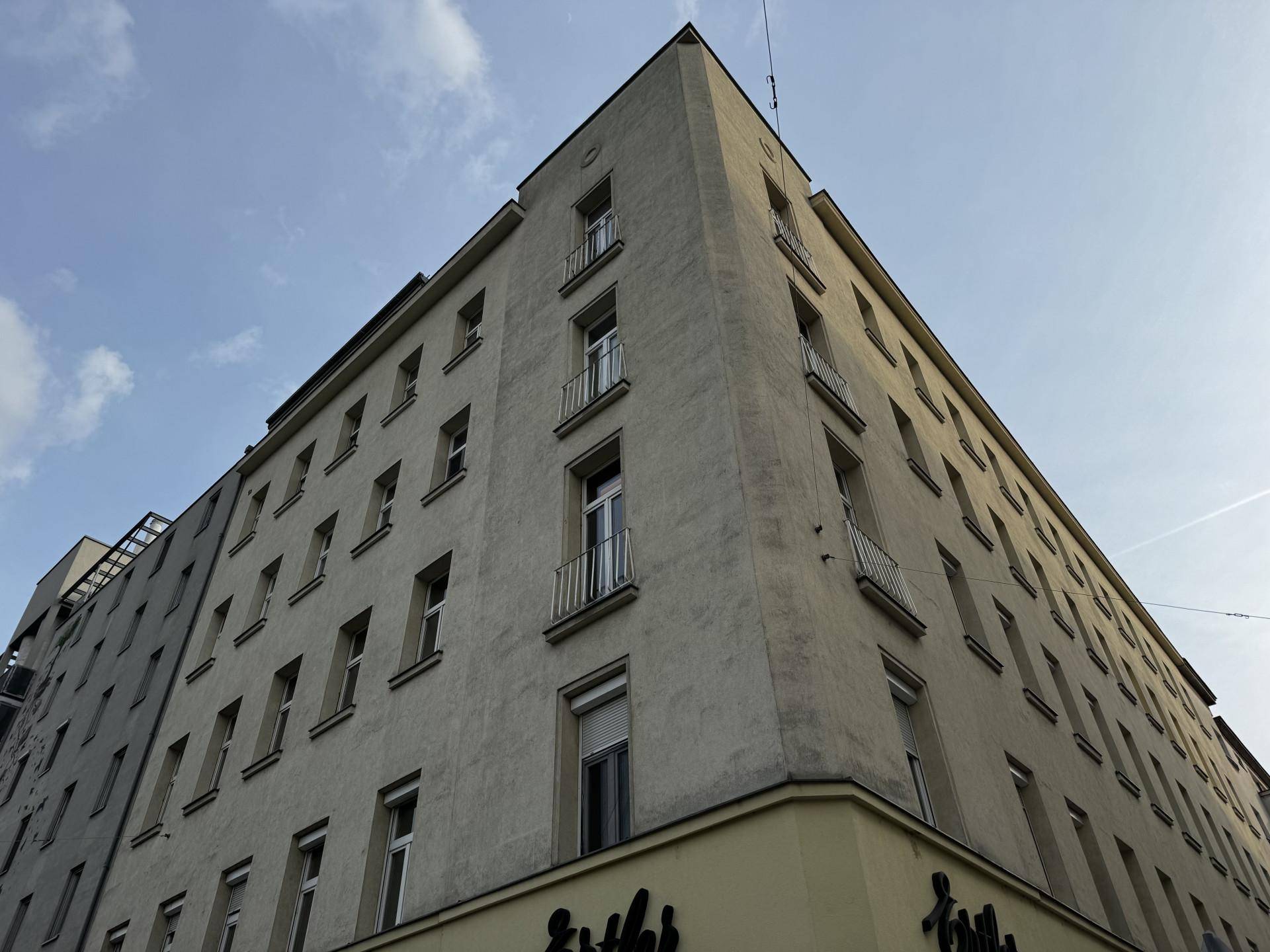 Eckgebäude mit mehreren Stockwerken und kleinen französischen Balkonen unter bewölktem Himmel.