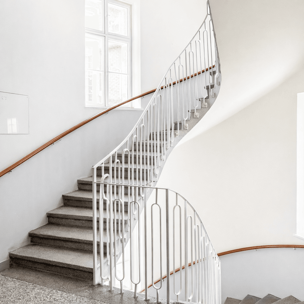 Elegantes Treppenhaus mit geschwungenem Geländer und Steinstufen in einem Altbau.
