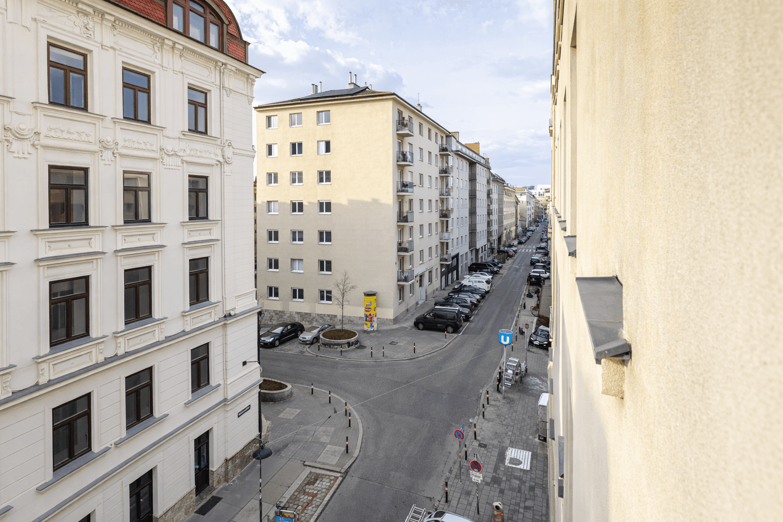 Blick von oben auf eine belebte Stadtstraße mit parkenden Autos und Gebäuden.
