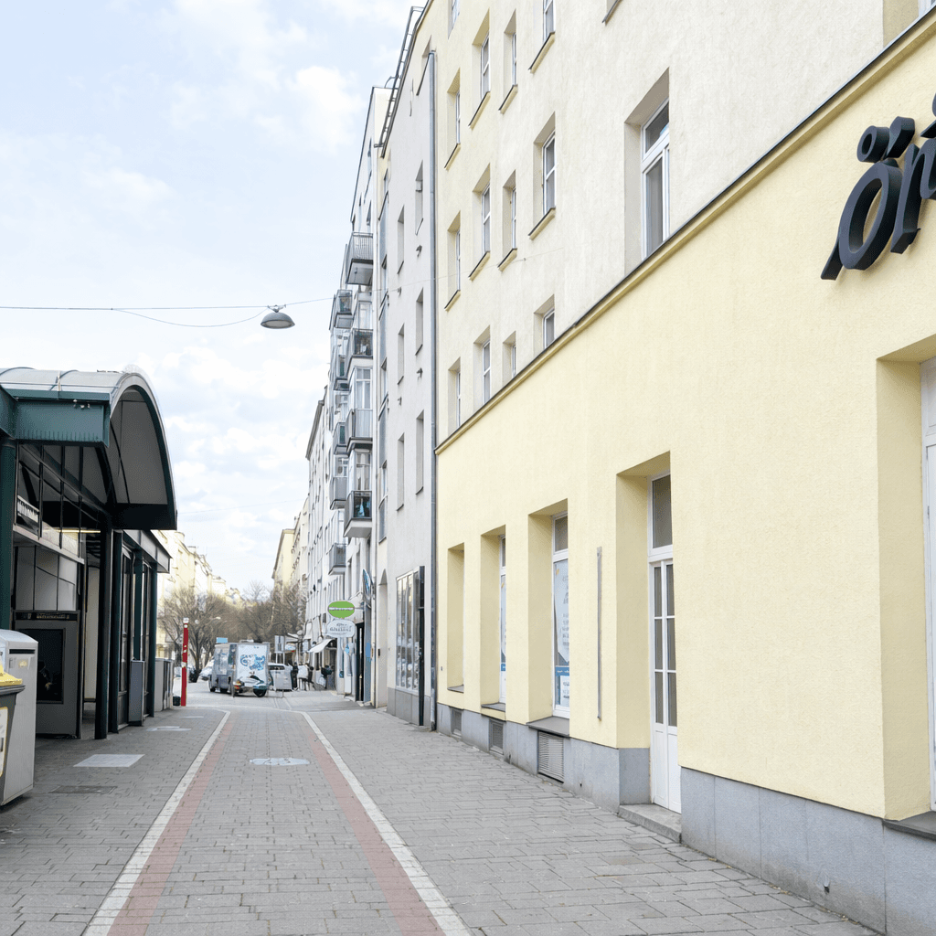 Eine ruhige Stadtstraße mit Gebäuden, Geschäften und einem U-Bahn-Eingang.