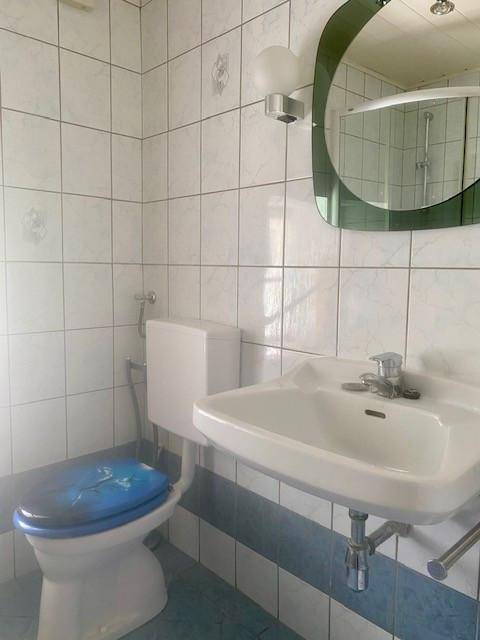 Badezimmer mit Waschbecken, WC und blauen Akzentfliesen.