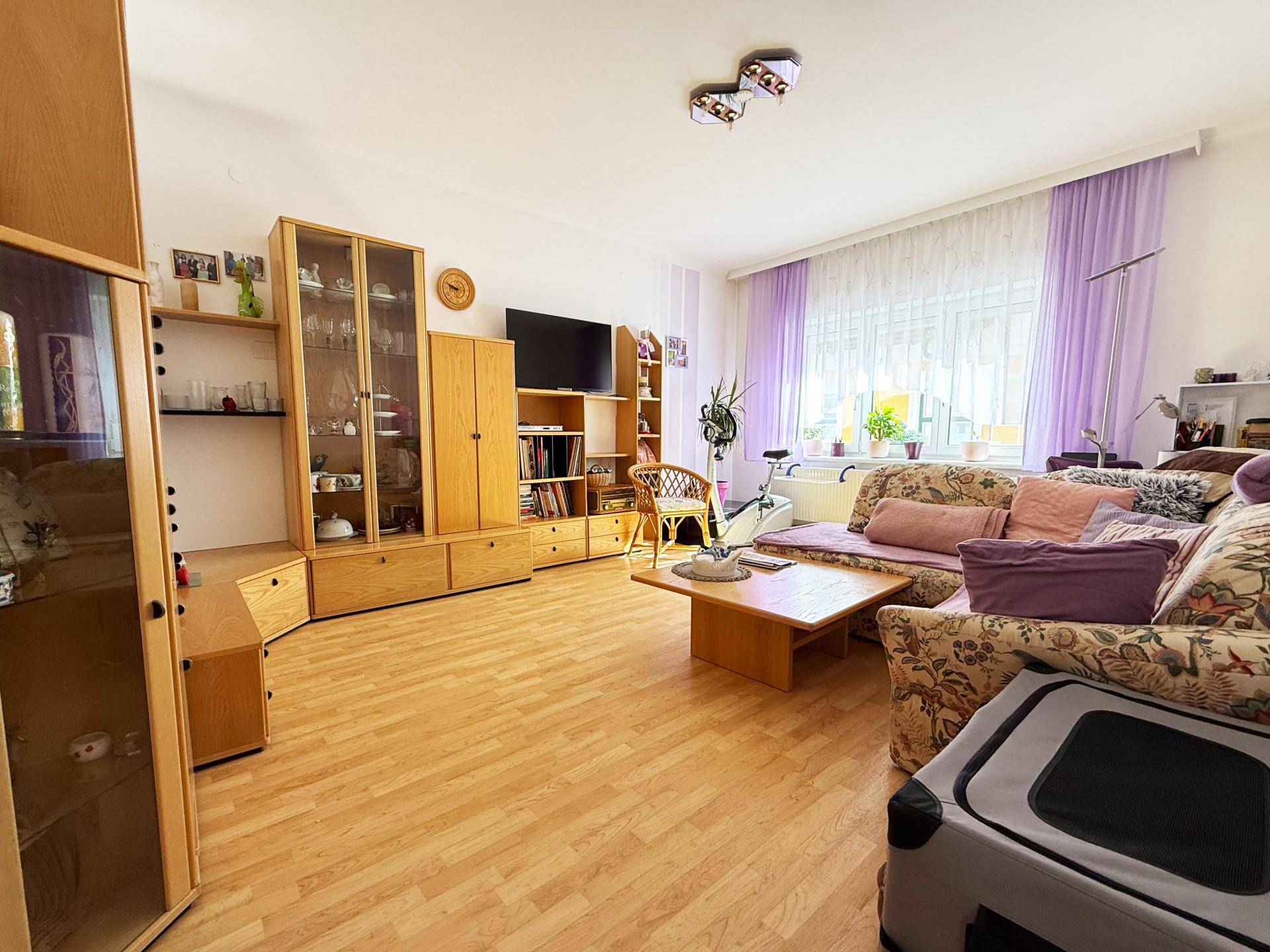 Geräumiges Wohnzimmer mit hellem Laminatboden, bequemer Couch und Holzmöbeln.