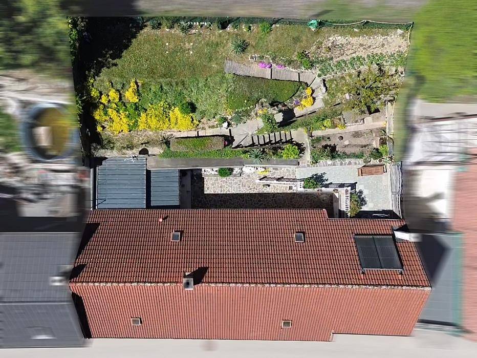 Draufsicht auf das Haus mit Ziegeldach, Solarpaneelen und dem terrassierten Garten.
