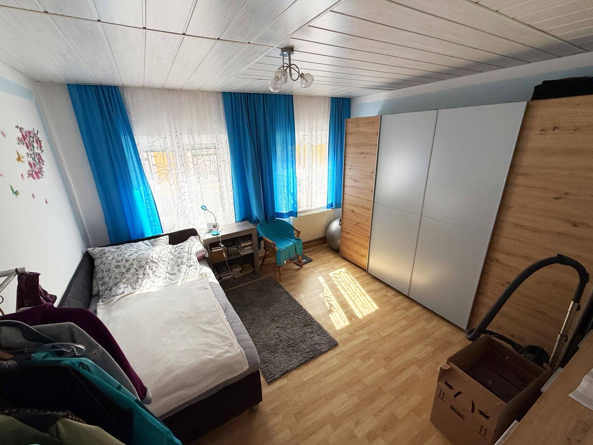 Schlafzimmer mit Einzelbett, großem Kleiderschrank und blauen Vorhängen.