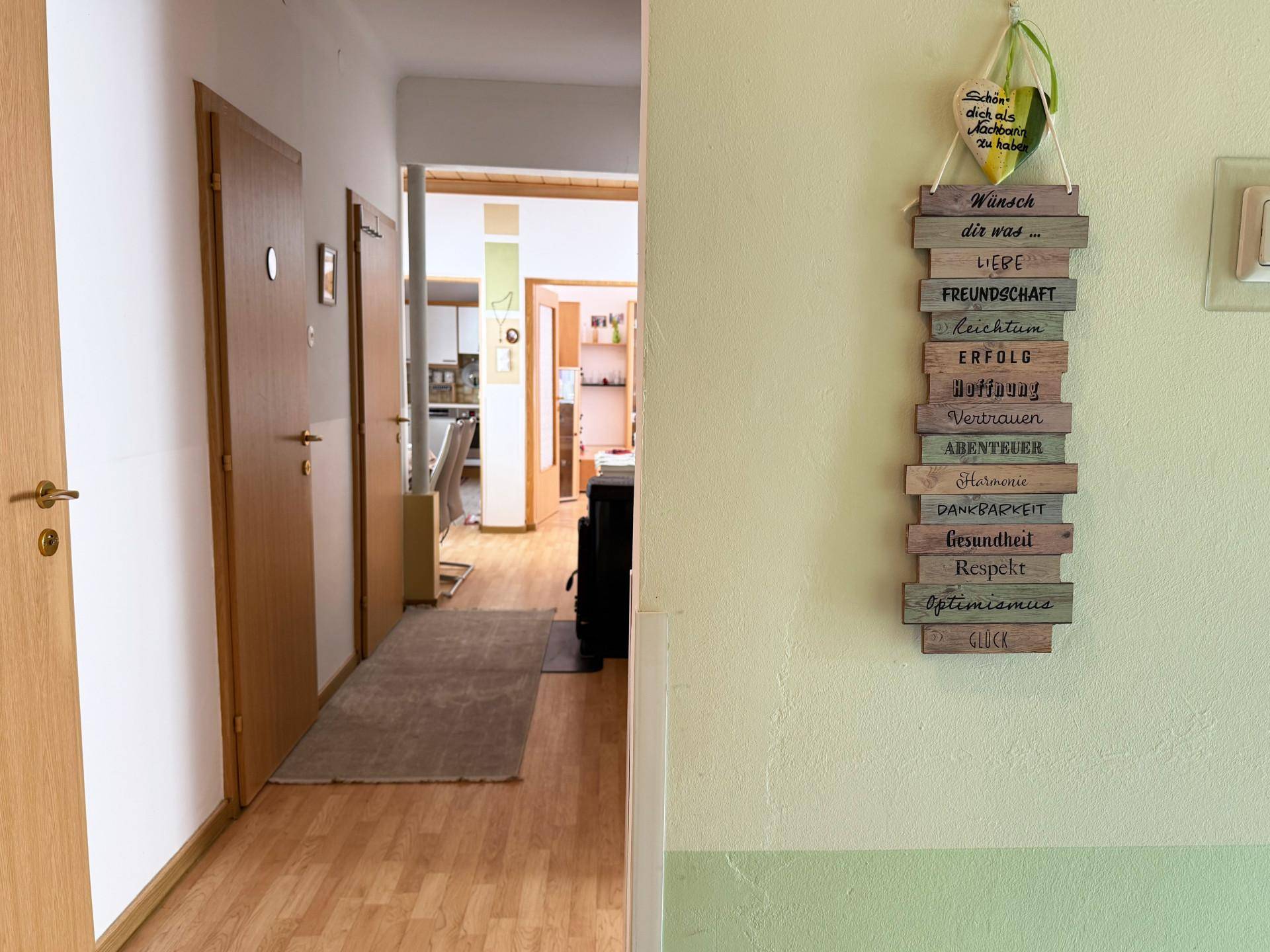 Flur mit Holztüren, hellem Laminatboden und einer dekorativen Wandtafel.