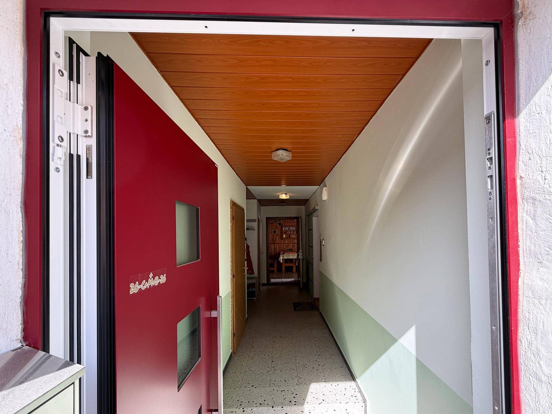 Eingangsbereich mit roter Haustür, Holzdecke und Terrazzoboden.