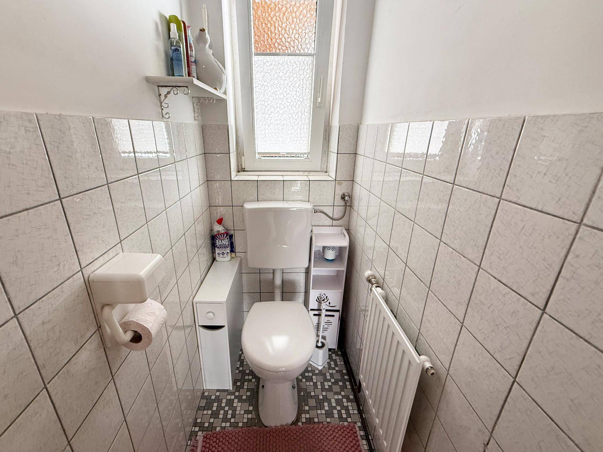 Kleines WC mit weißen Fliesen, Fenster und Heizkörper.