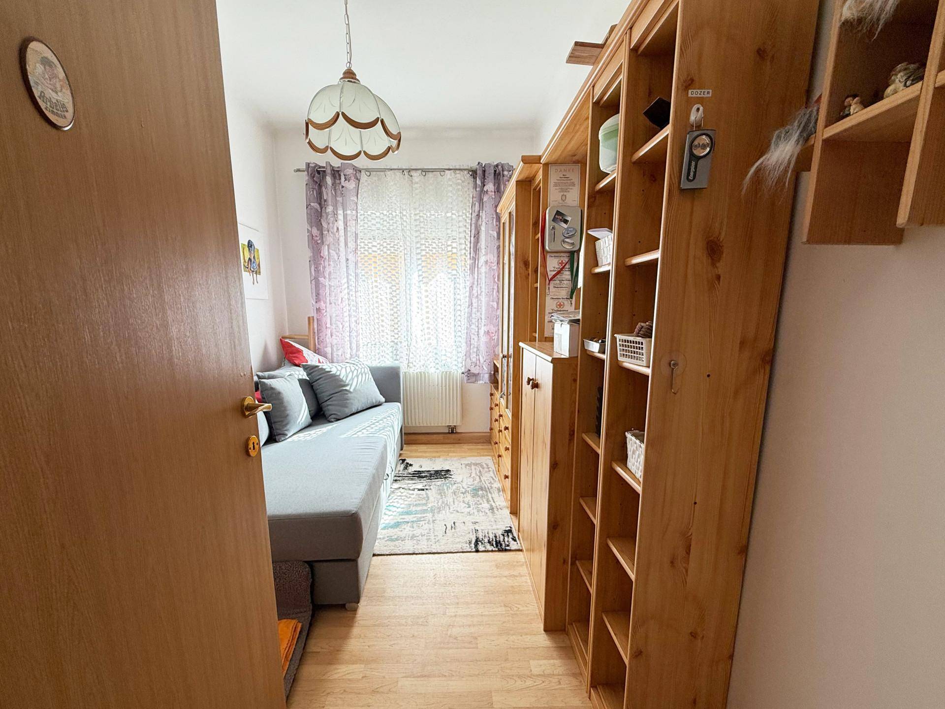 Kleines Zimmer mit Schlafsofa, Holzregalen und hellem Laminatboden.