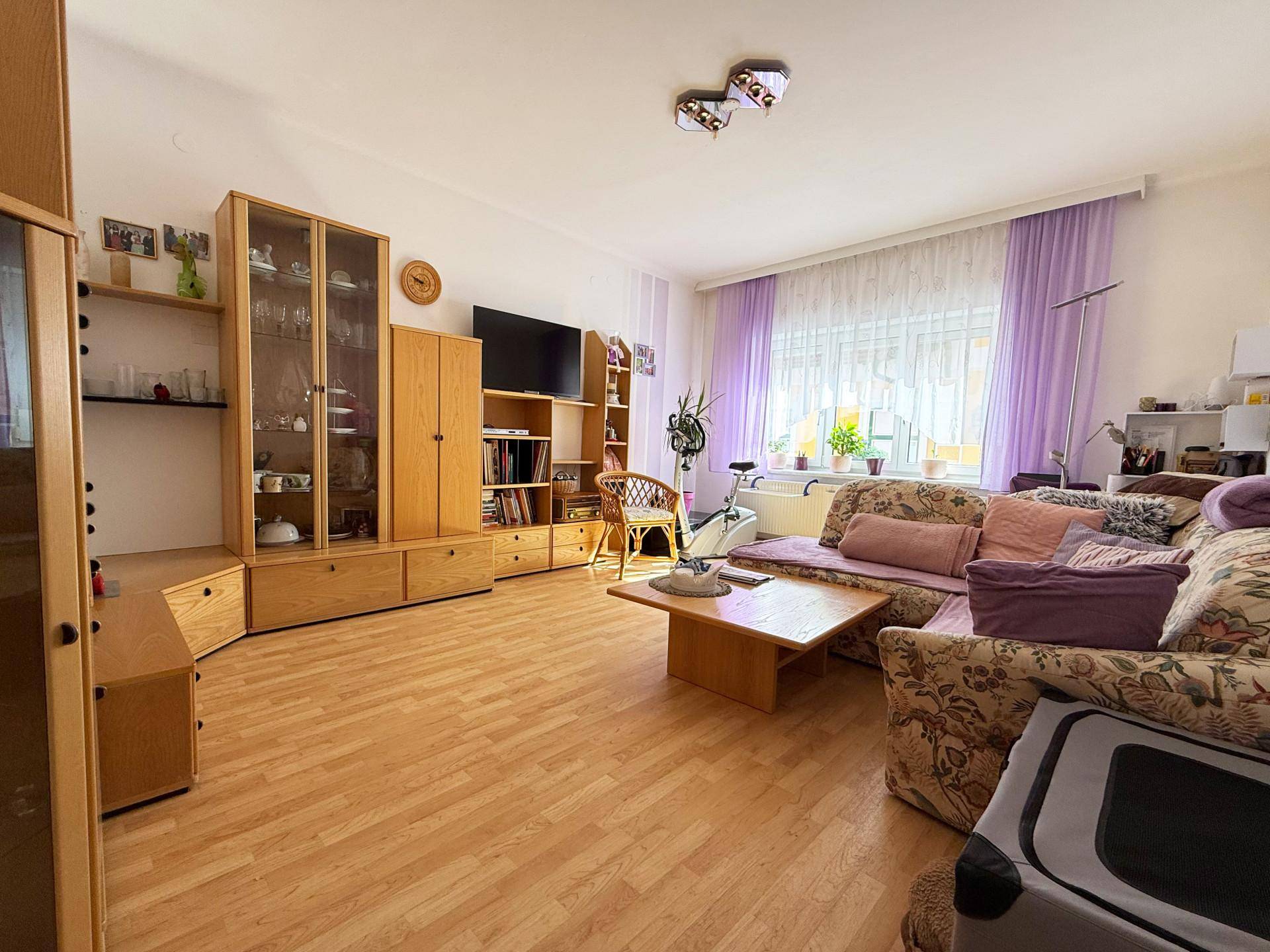 Geräumiges Wohnzimmer mit hellem Laminatboden, bequemer Couch und Holzmöbeln.