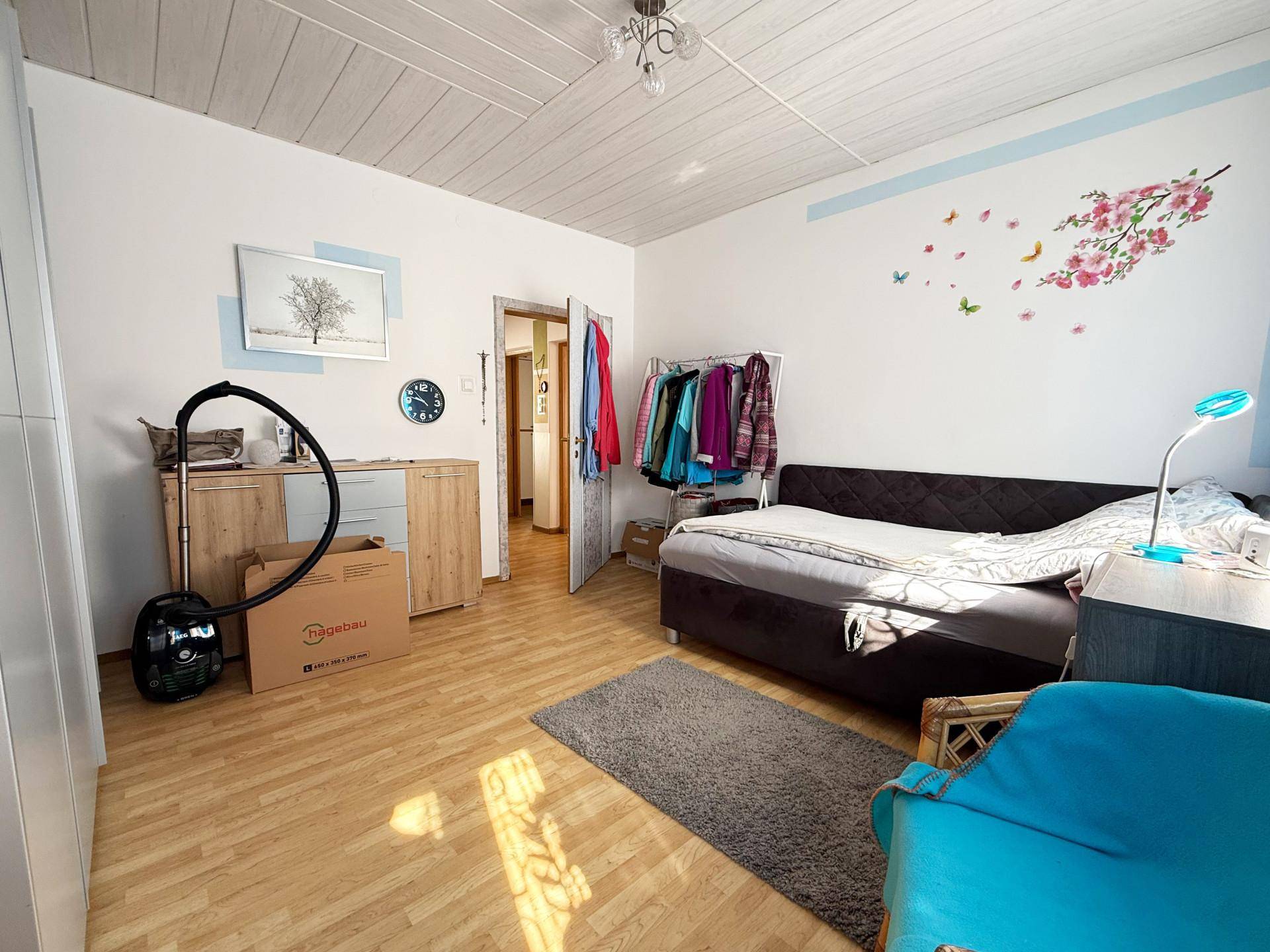 Schlafzimmer mit Doppelbett, Laminatboden und einem offenen Kleiderständer.