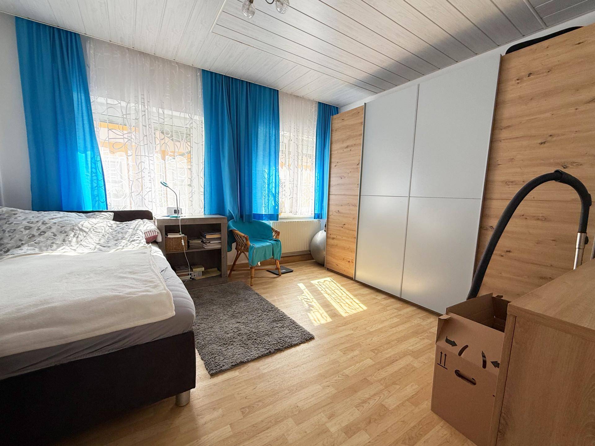 Schlafzimmer mit Einzelbett, großem Kleiderschrank und blauen Vorhängen.
