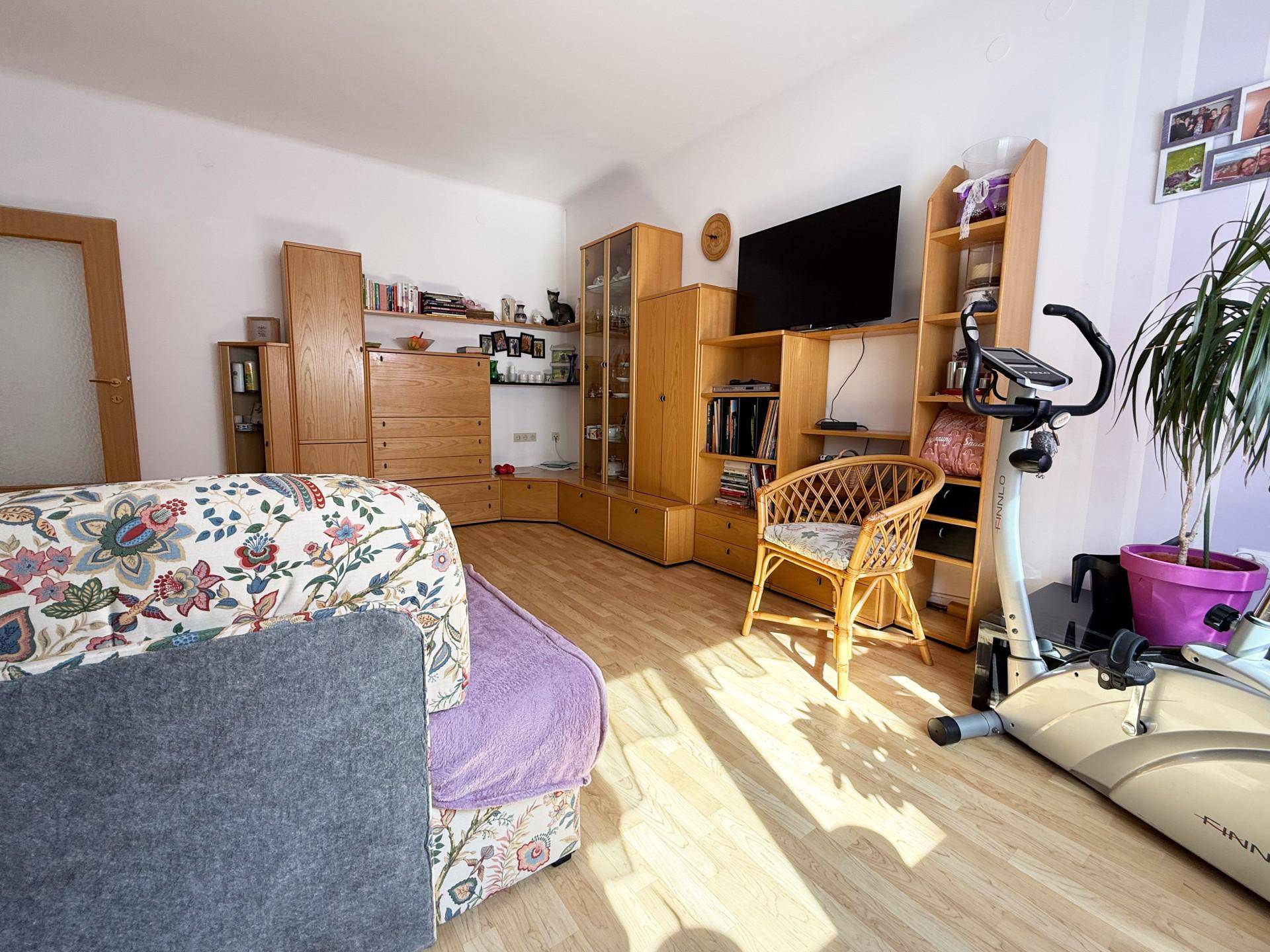 Wohnzimmer mit Laminatboden, großer Couch und einem Heimtrainer.