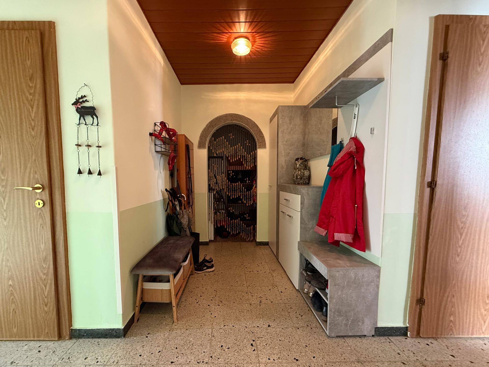 Eingangsbereich mit Terrazzoboden, Holzdecke und Garderobe.