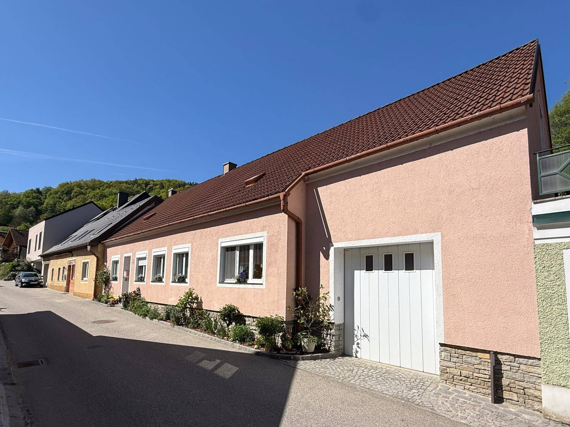 Ansicht des Hauses von der Straße mit rosafarbener Fassade und weißem Garagentor.