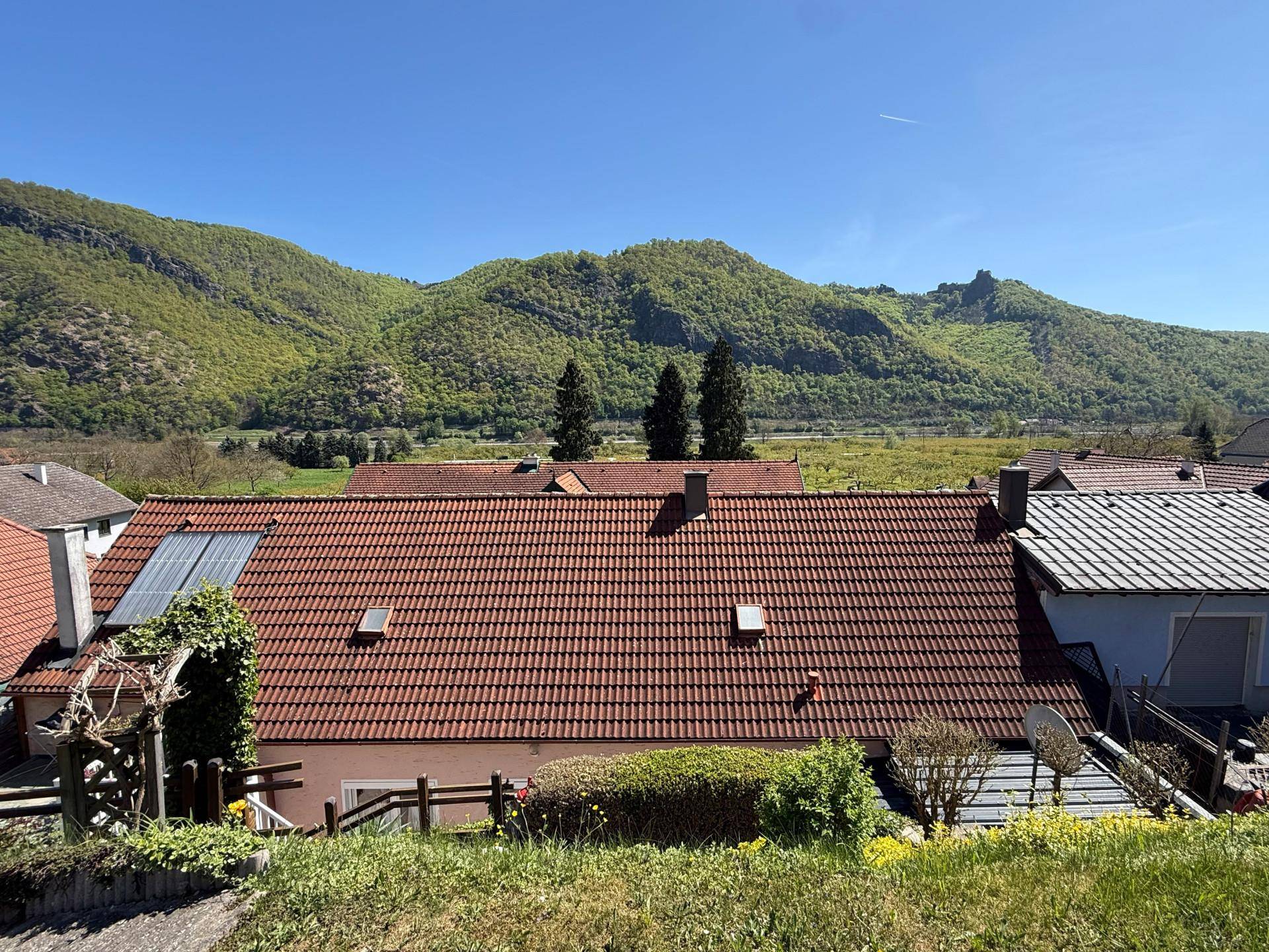 Panoramablick auf das Haus mit Ziegeldach, Solarpaneelen und grüner Berglandschaft im Hintergrund.